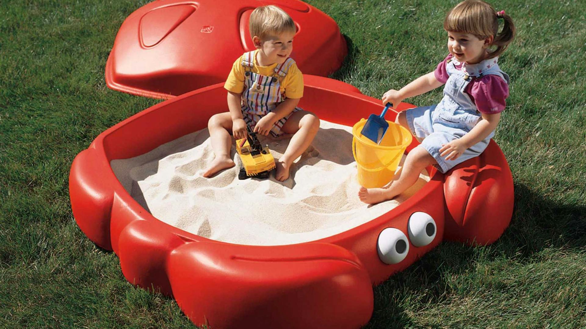 Zwei Kinder spielen im roten Kunststoff-Sandkasten.