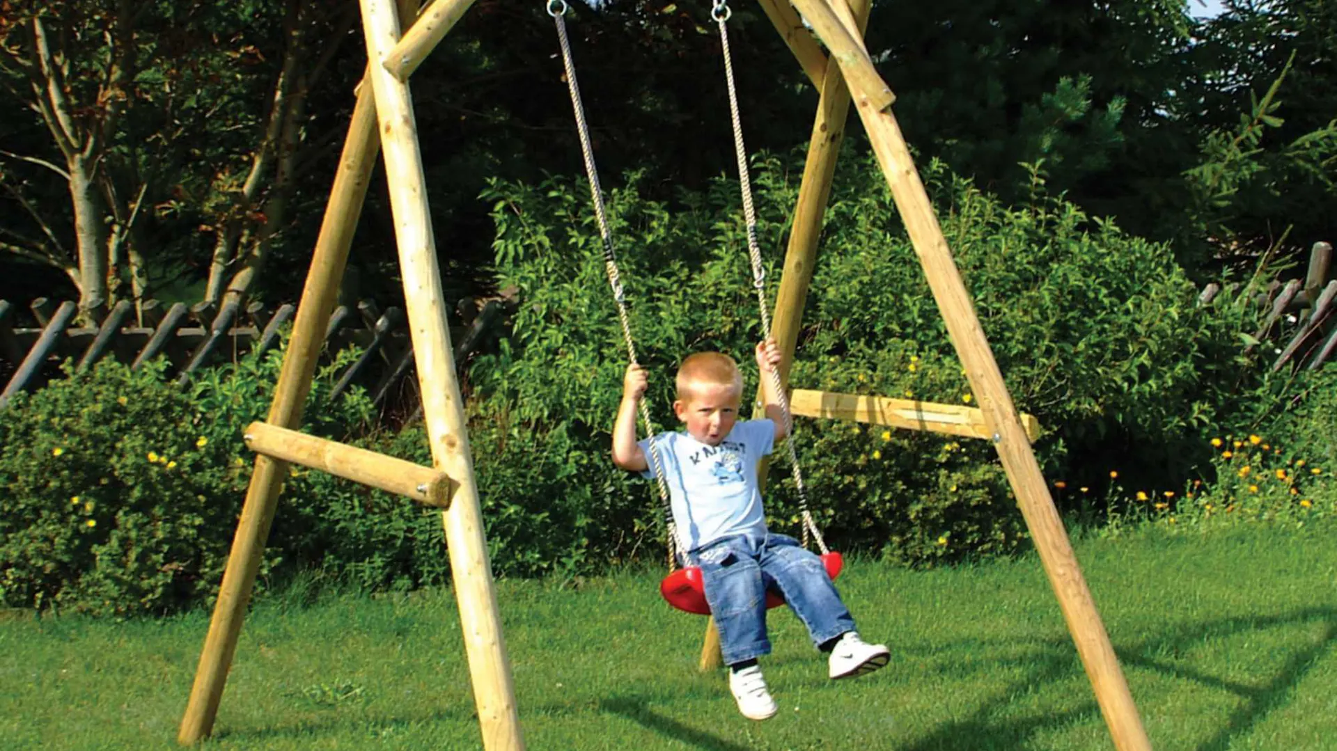 Un bambino dondola su un’altalena rossa con telaio in legno in giardino.