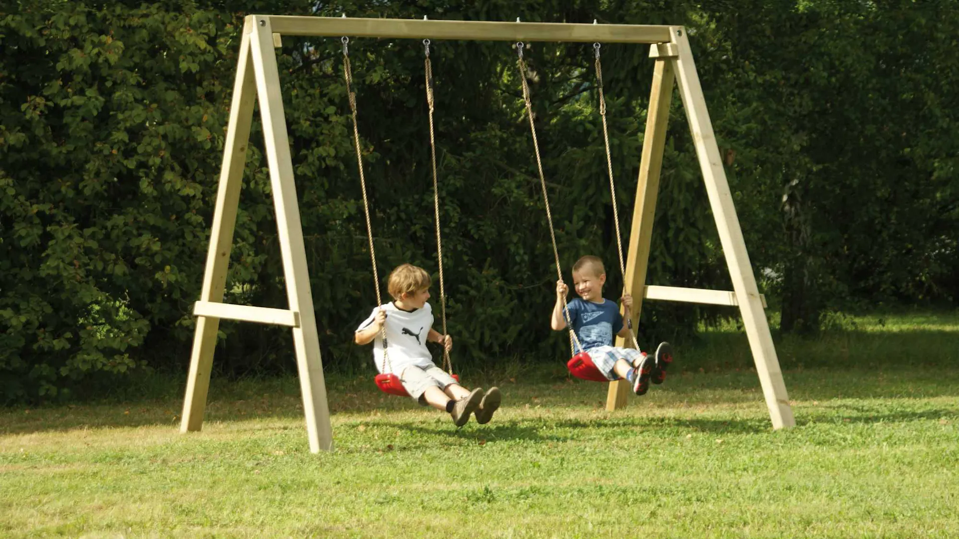 Due bambini in altalena su due altalene rosse sul telaio di legno in giardino.
