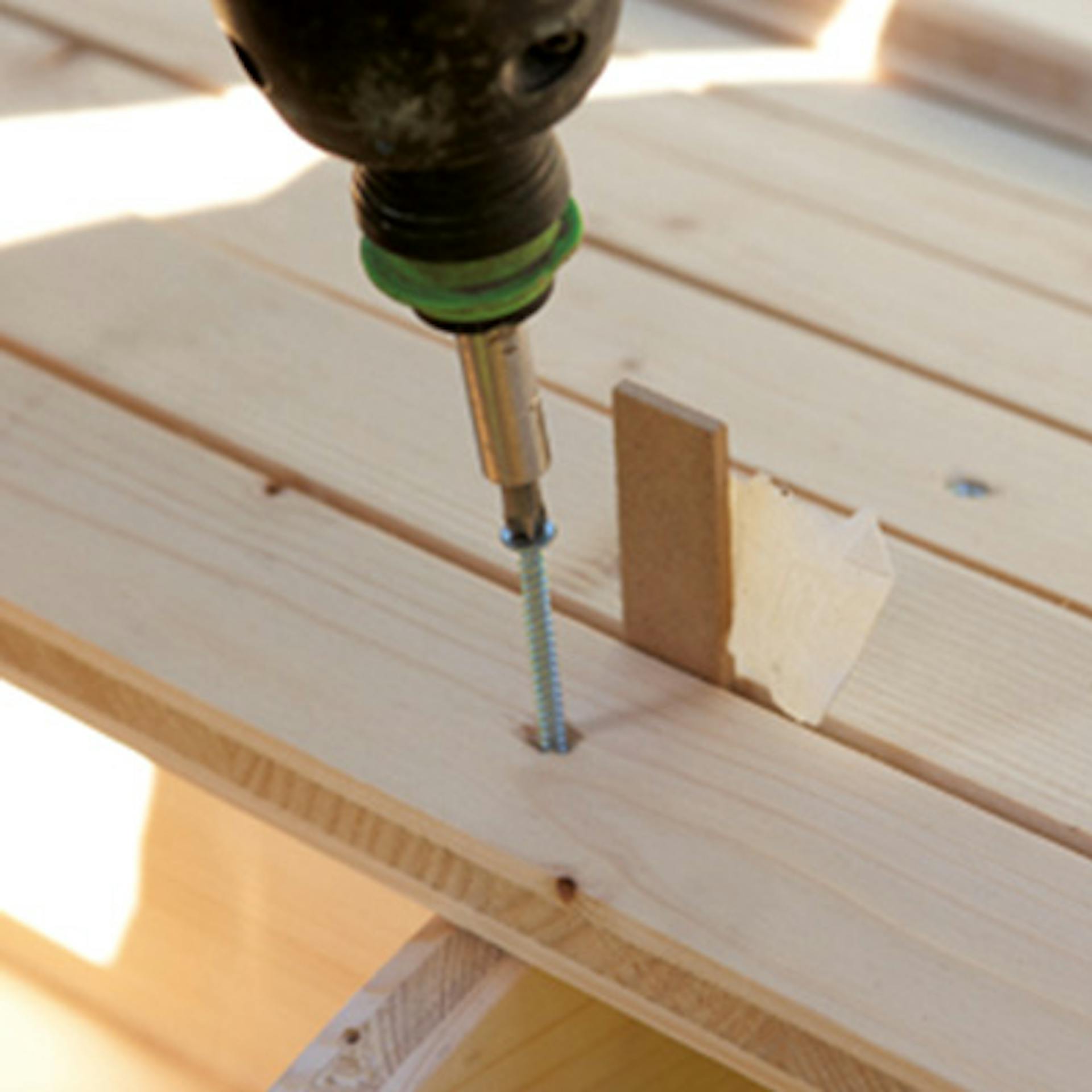 Person schraubt Holzleisten mithilfe von Abstandshalter und Akkuschrauber auf Formspanten auf.