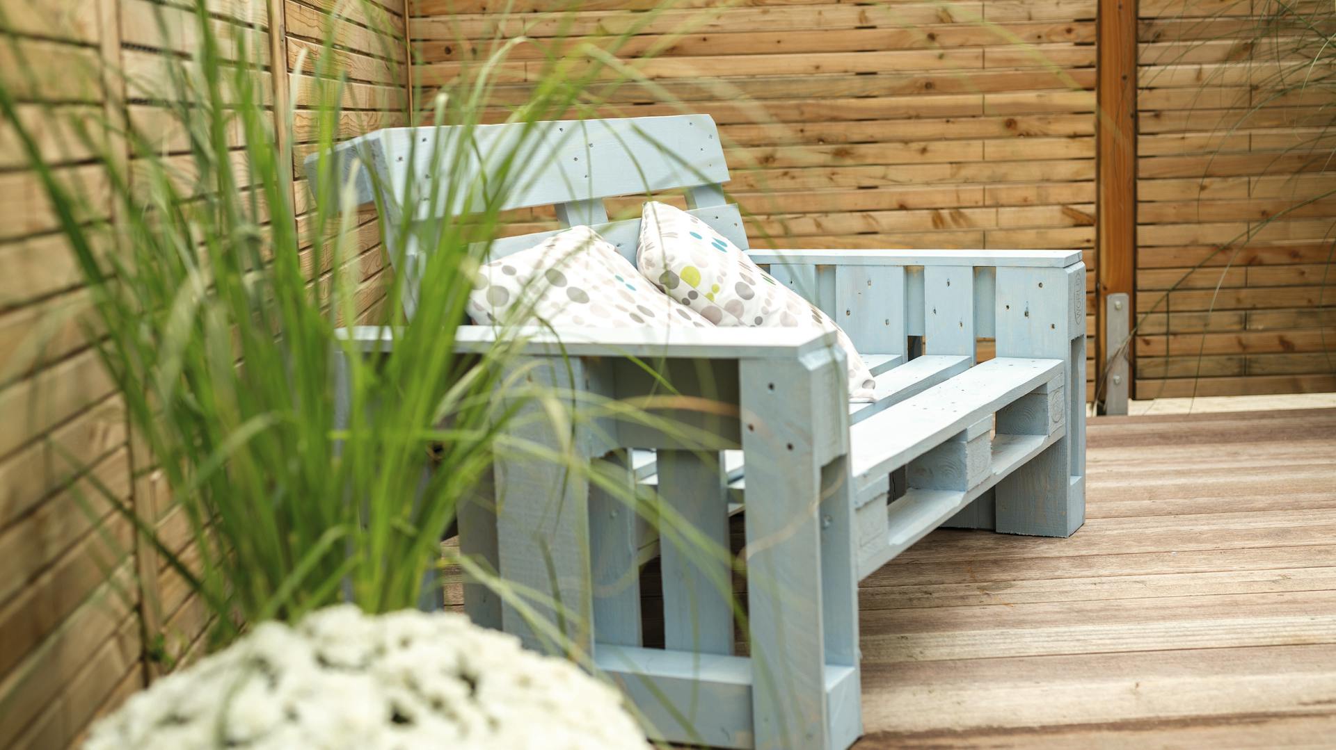Hellblau gestrichene Paletten Couch mit Armlehnen auf Holzterrasse mit Deko