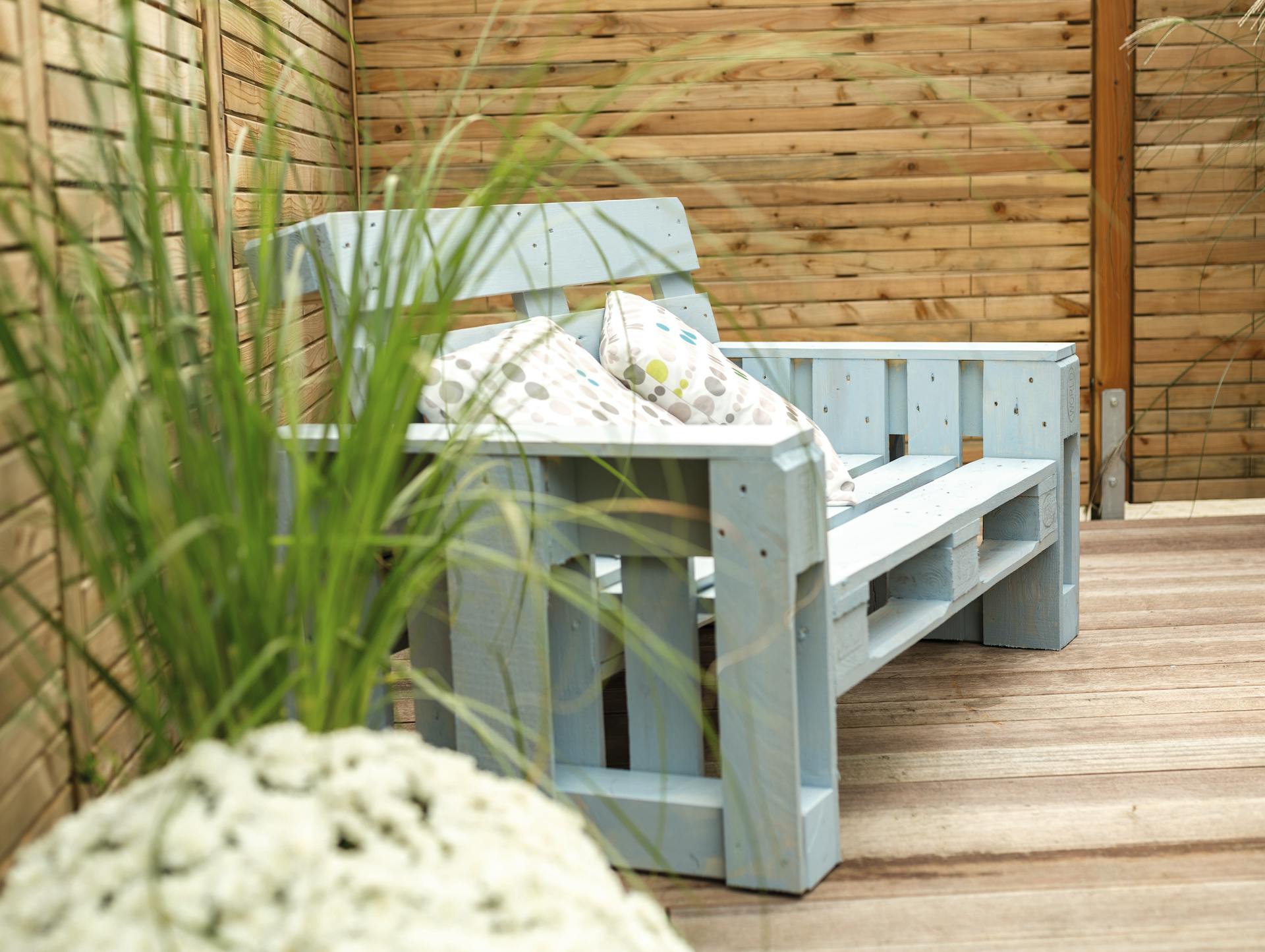 Canapé en palettes peint en bleu clair avec accoudoirs sur terrasse en bois avec déco