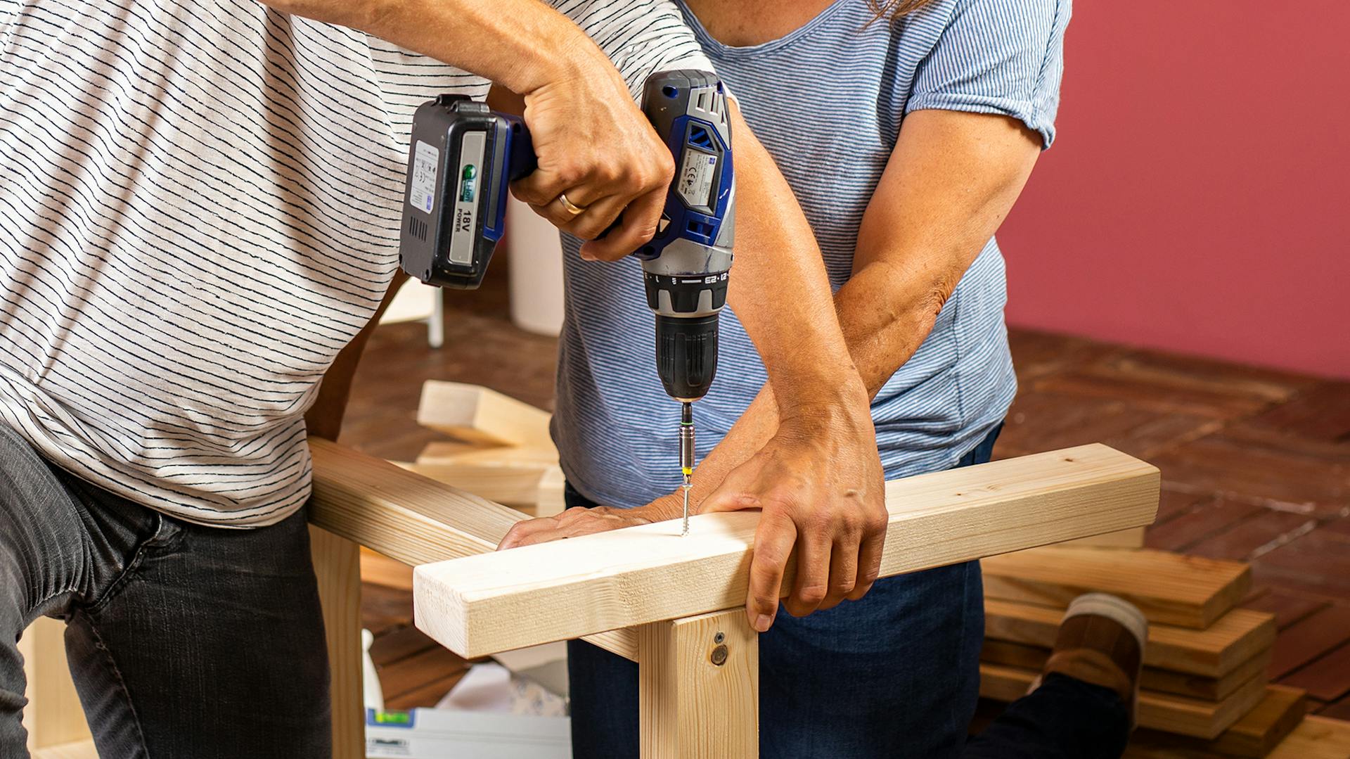 Due persone avvitano insieme una panca: una persona avvita, l’altra mantiene le parti in legno in posizione.