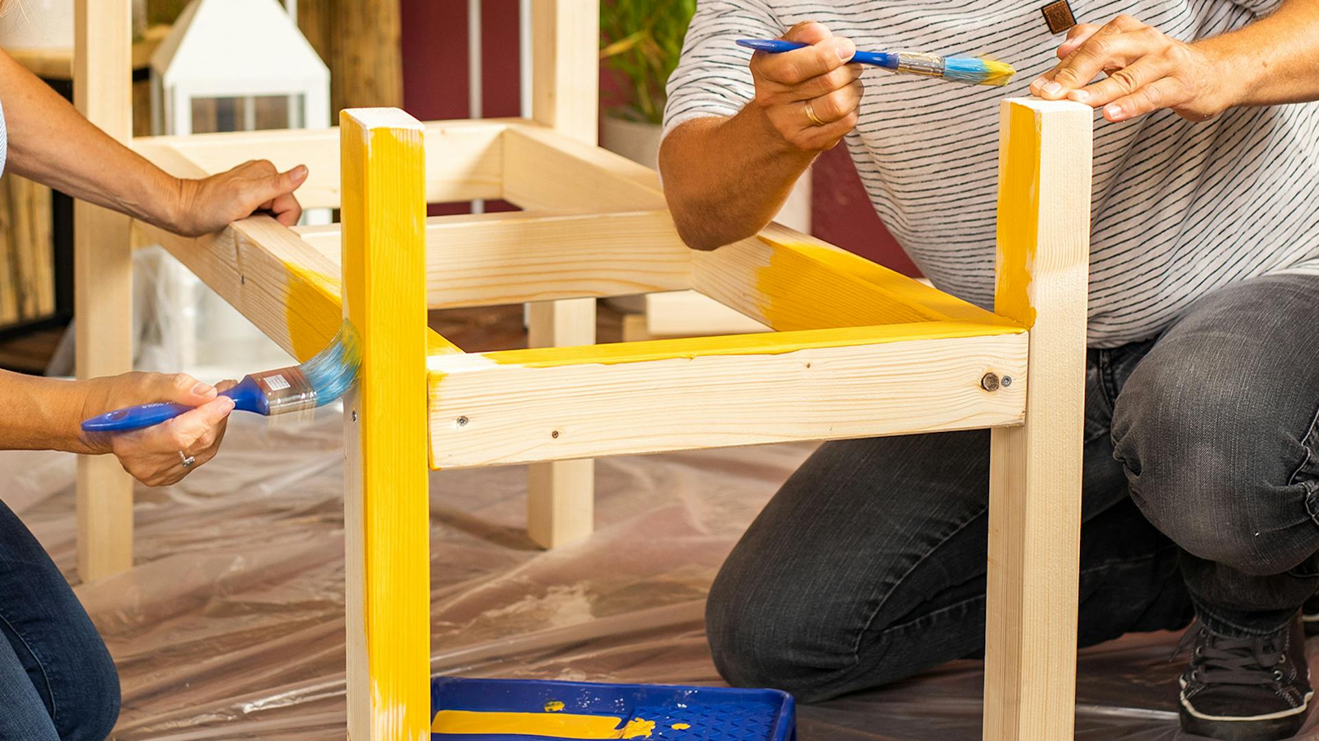 Due persone verniciano una panca fai da te di legno di colore giallo