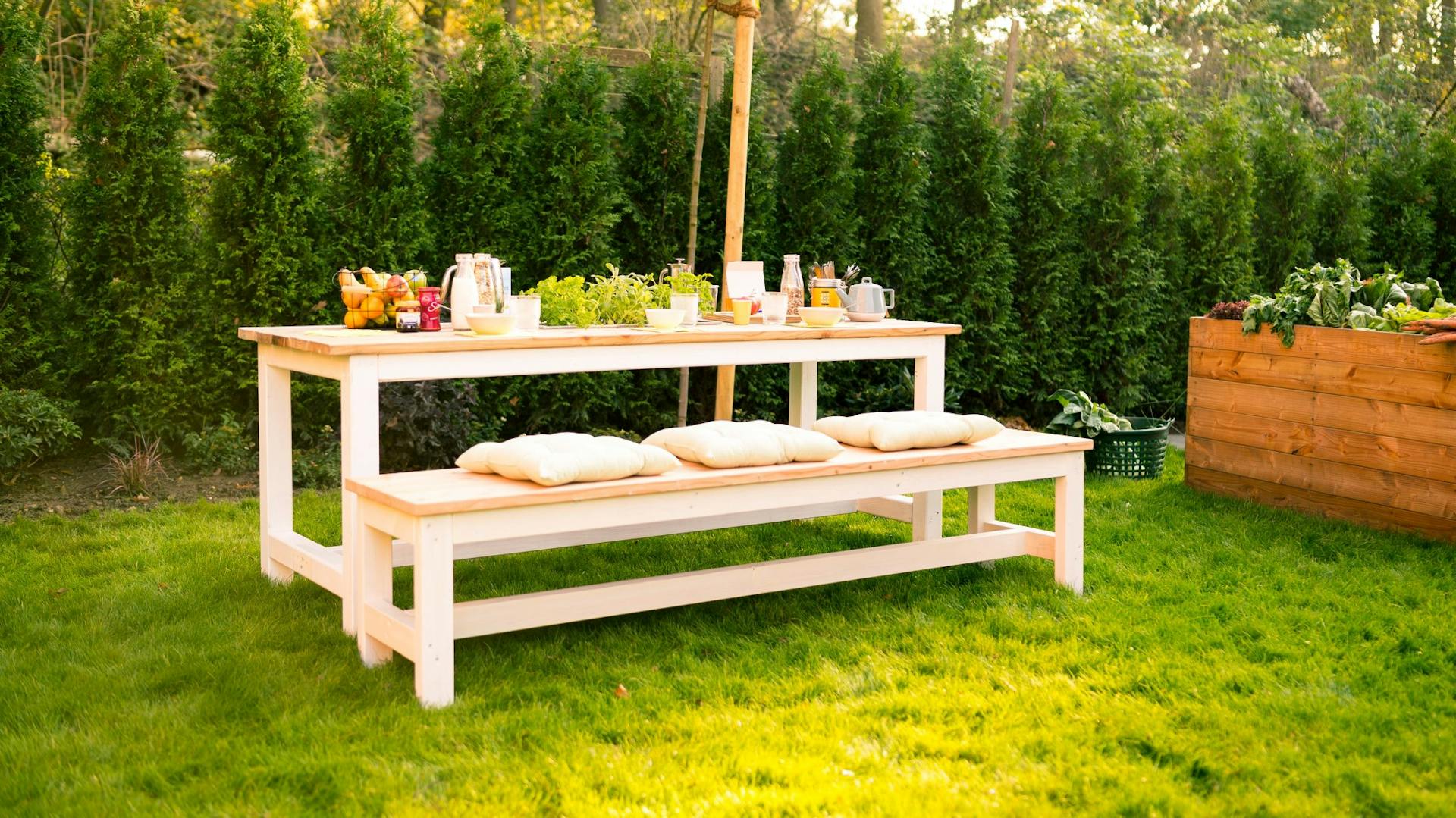 Panca fai da te con cuscini davanti a un tavolo coperto sul prato in giardino