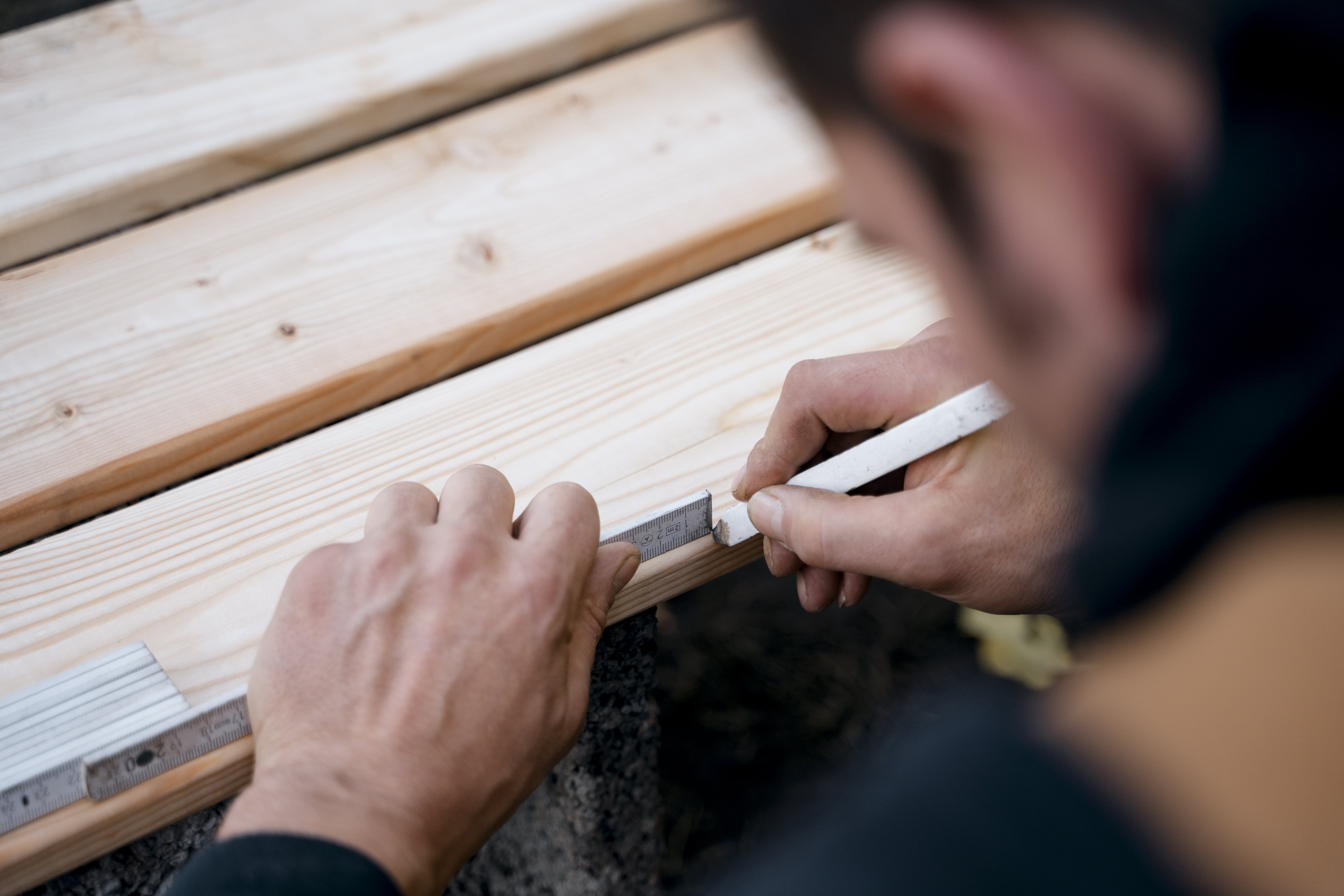 Heimwerker markiert Sägestelle auf Holz.