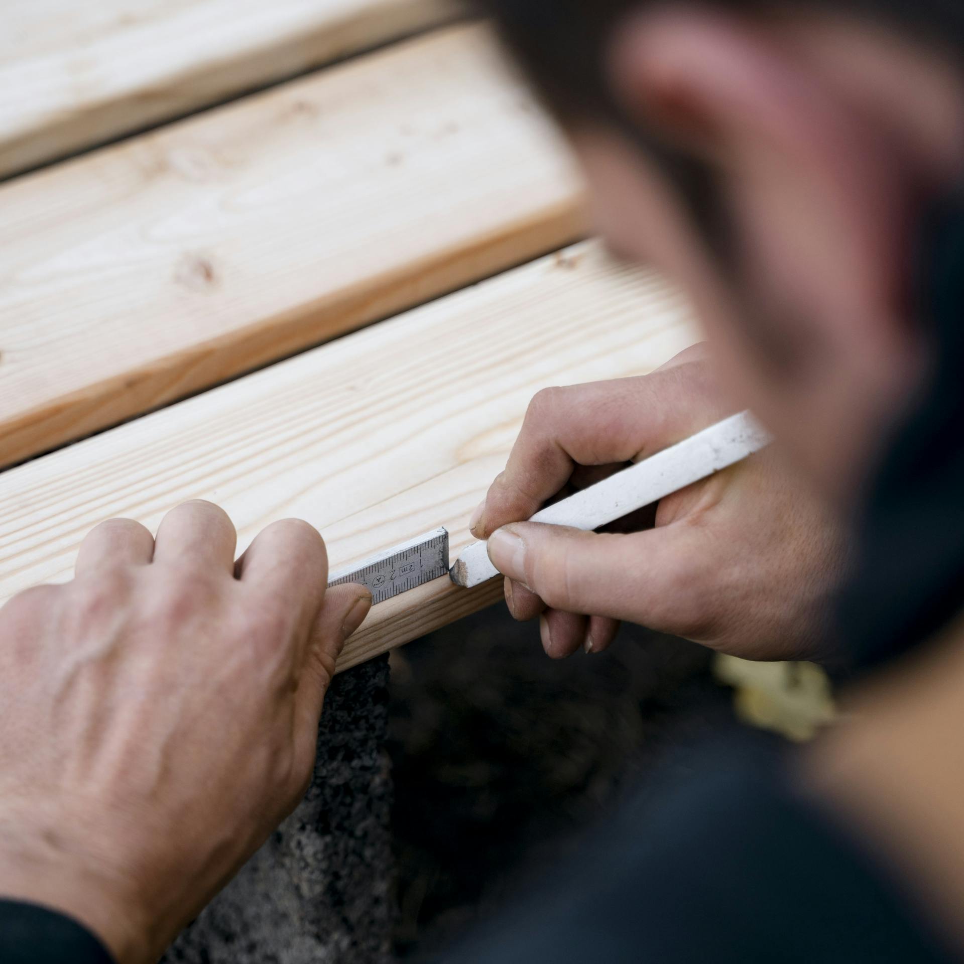 Heimwerker markiert Sägestelle auf Holz.
