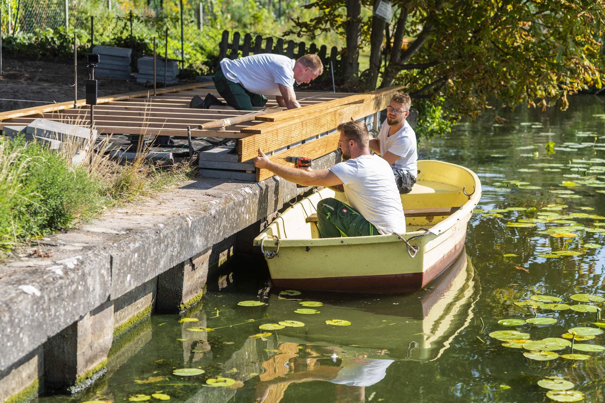 Männer montieren Terrassendielen von einem Boot aus.