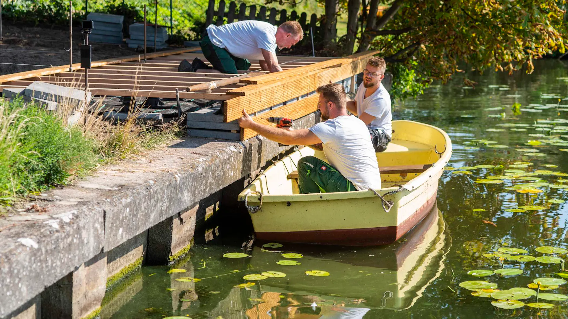 Männer montieren Terrassendielen von einem Boot aus.