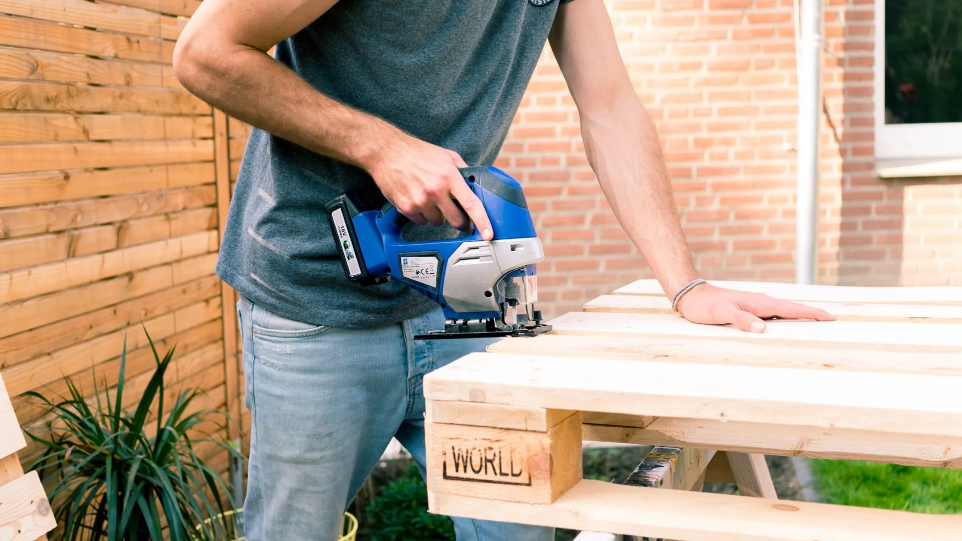 Person sägt Palette für den Bau von Gartenmöbeln zurecht.
