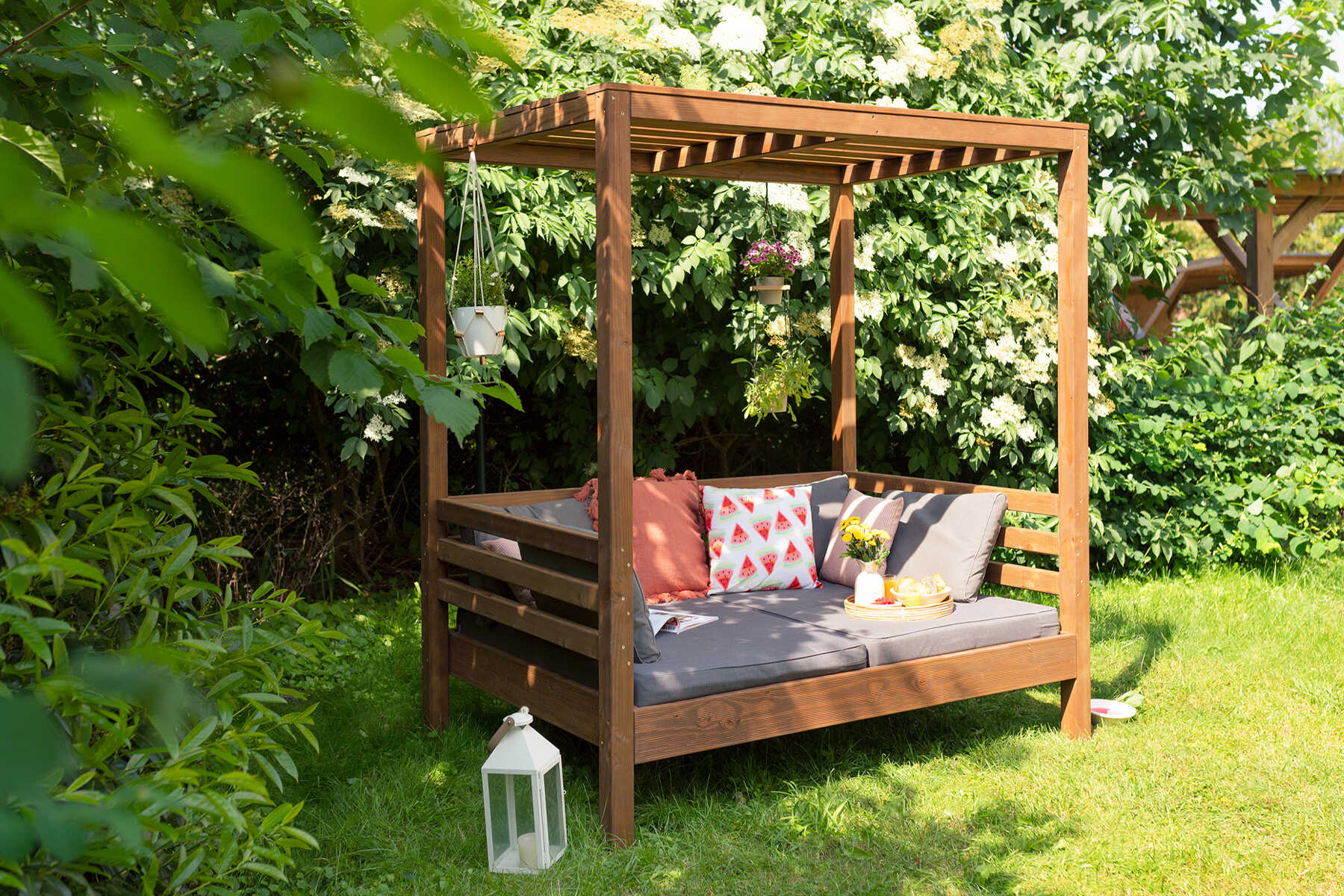Seitliche Ansicht der aus Vollholz selbstgebauten Sonneninsel Helena in in dunkler Holzfarbe mit Sitzpolstern für zwei Personen.