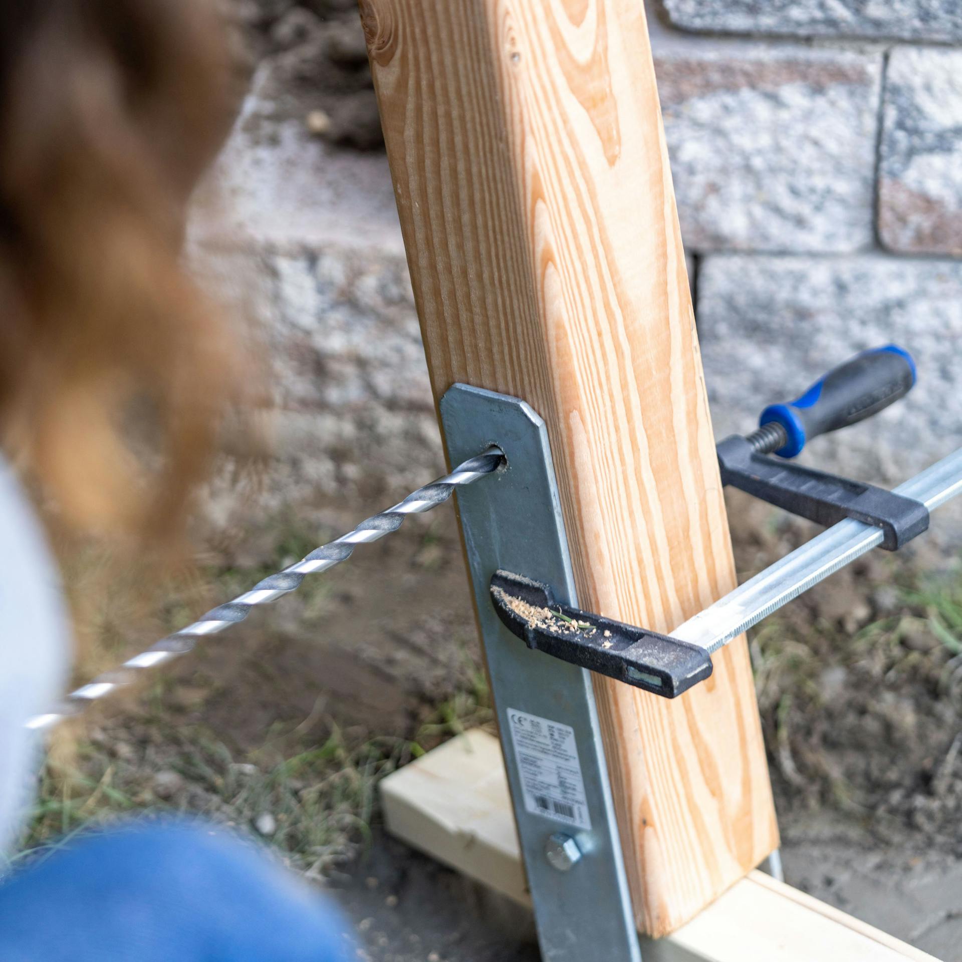 Langer Bohrer, der durch einen H-Anker und einen Holzpfosten bohrt