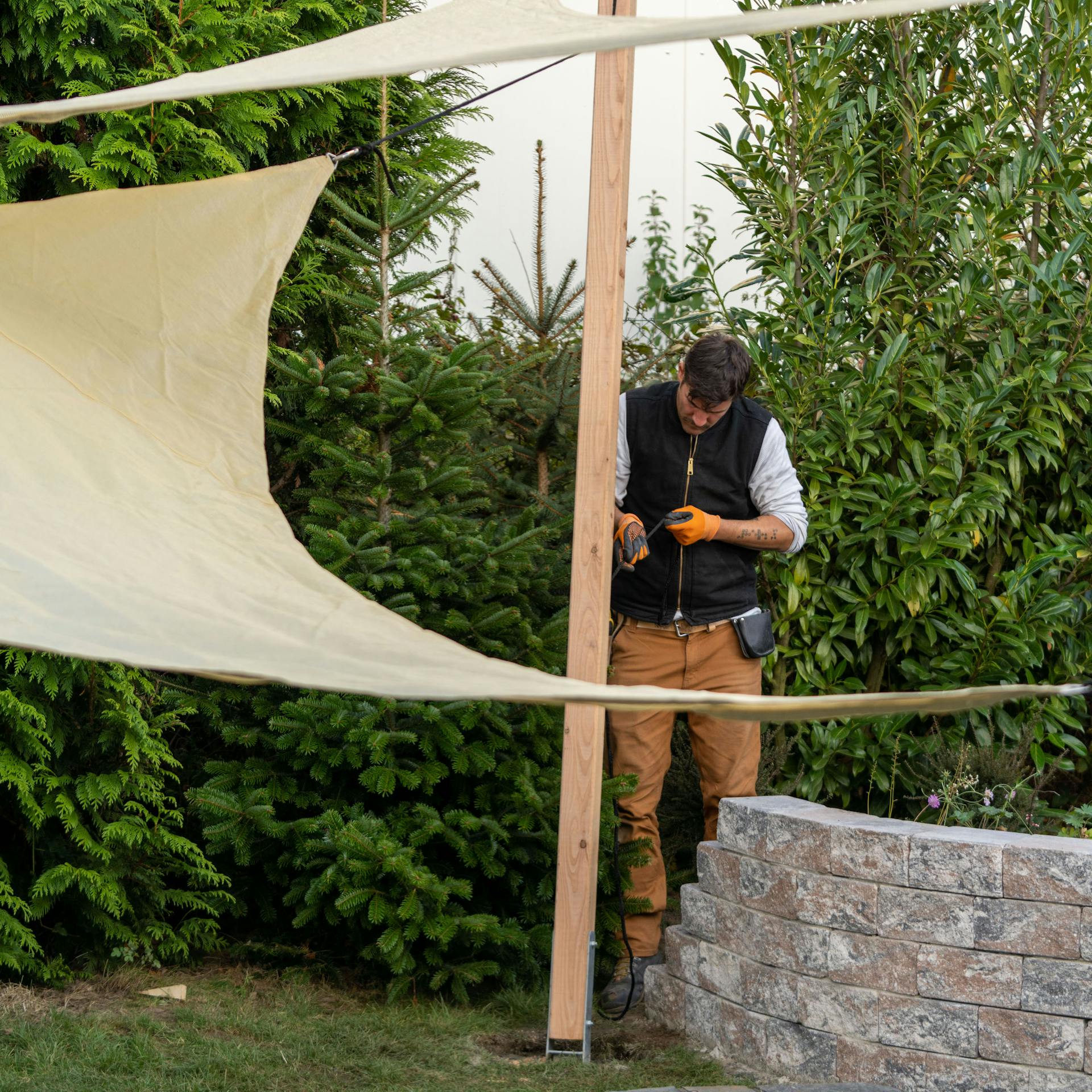 Mann befestigt Seil eines Sonnensegels an einem Holzpfosten
