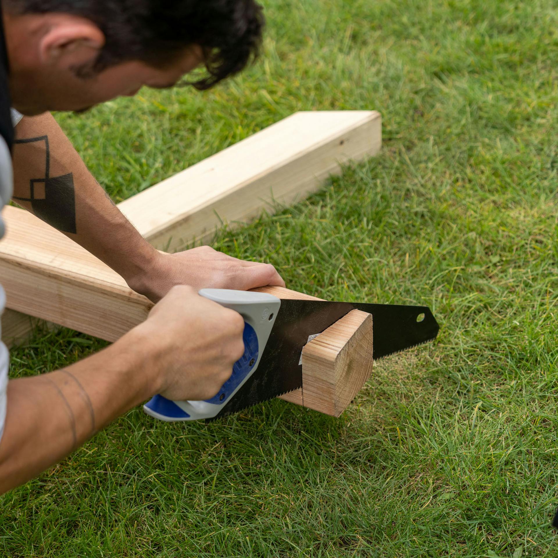 Mann sägt mit einer Handsäge einen Holzpfosten ab