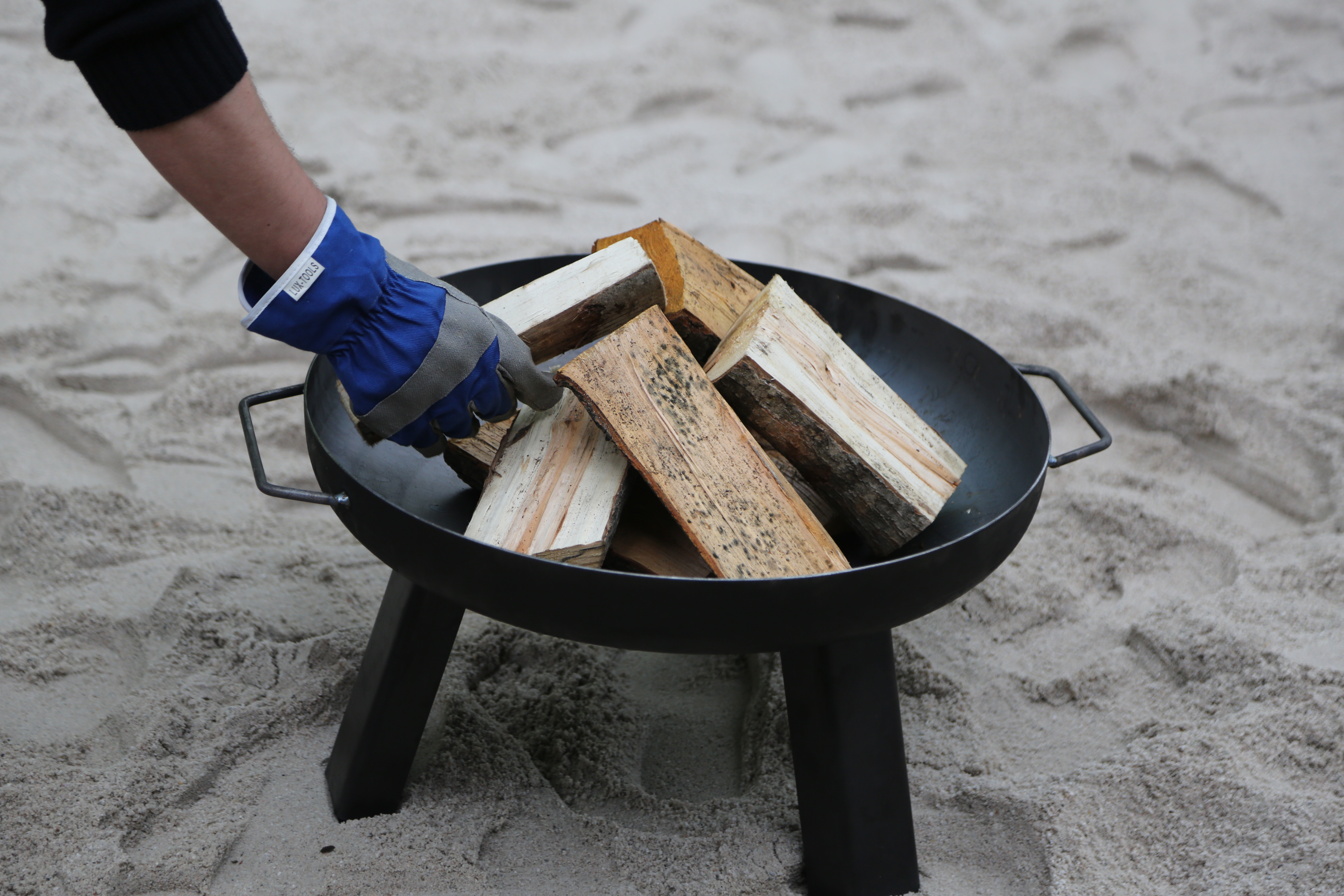 Hand legt Holzscheit in Feuerschale