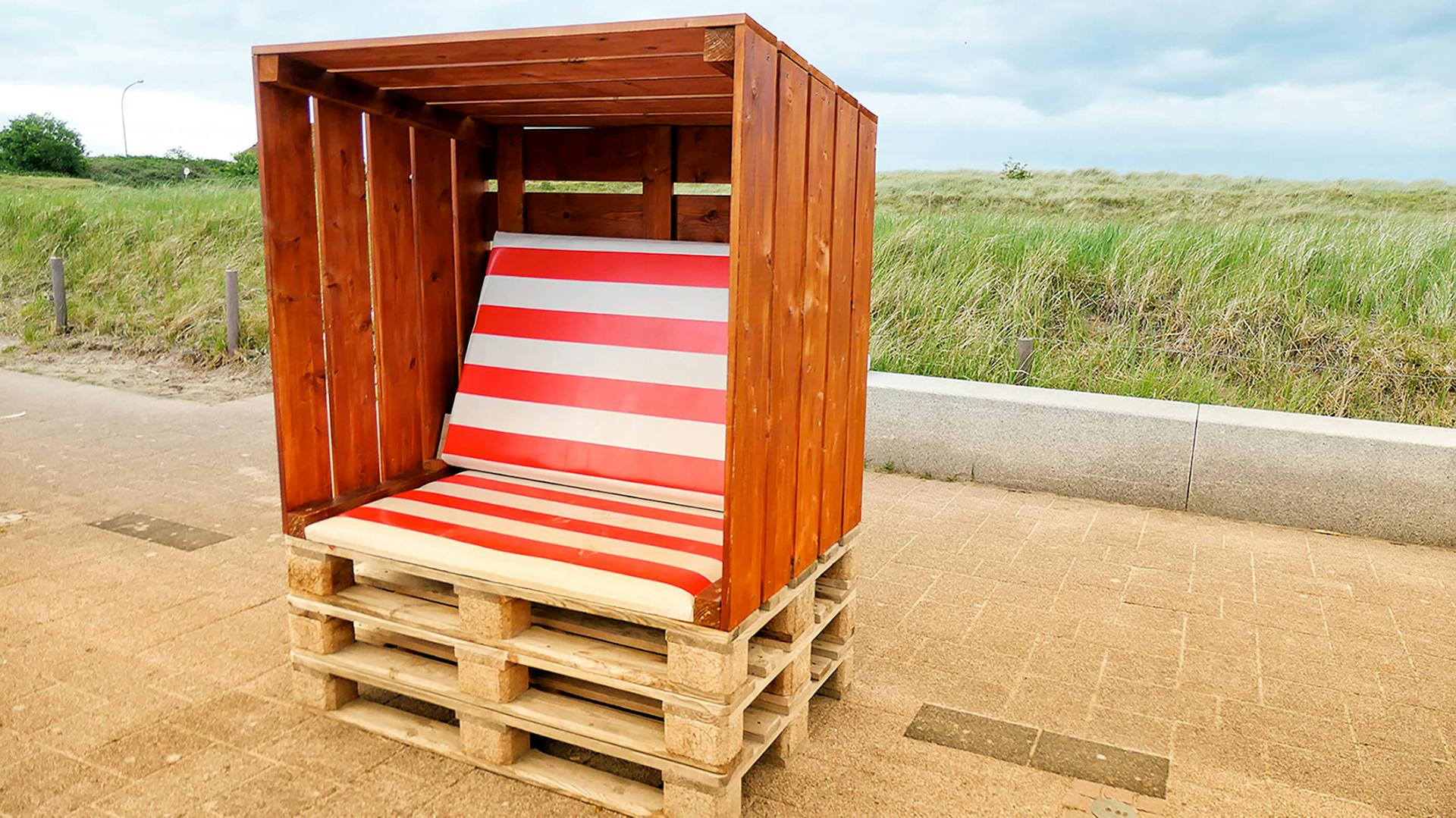 Aus Paletten gebauter Strandkorb mit weiß rot gestreiftem Kissen.
