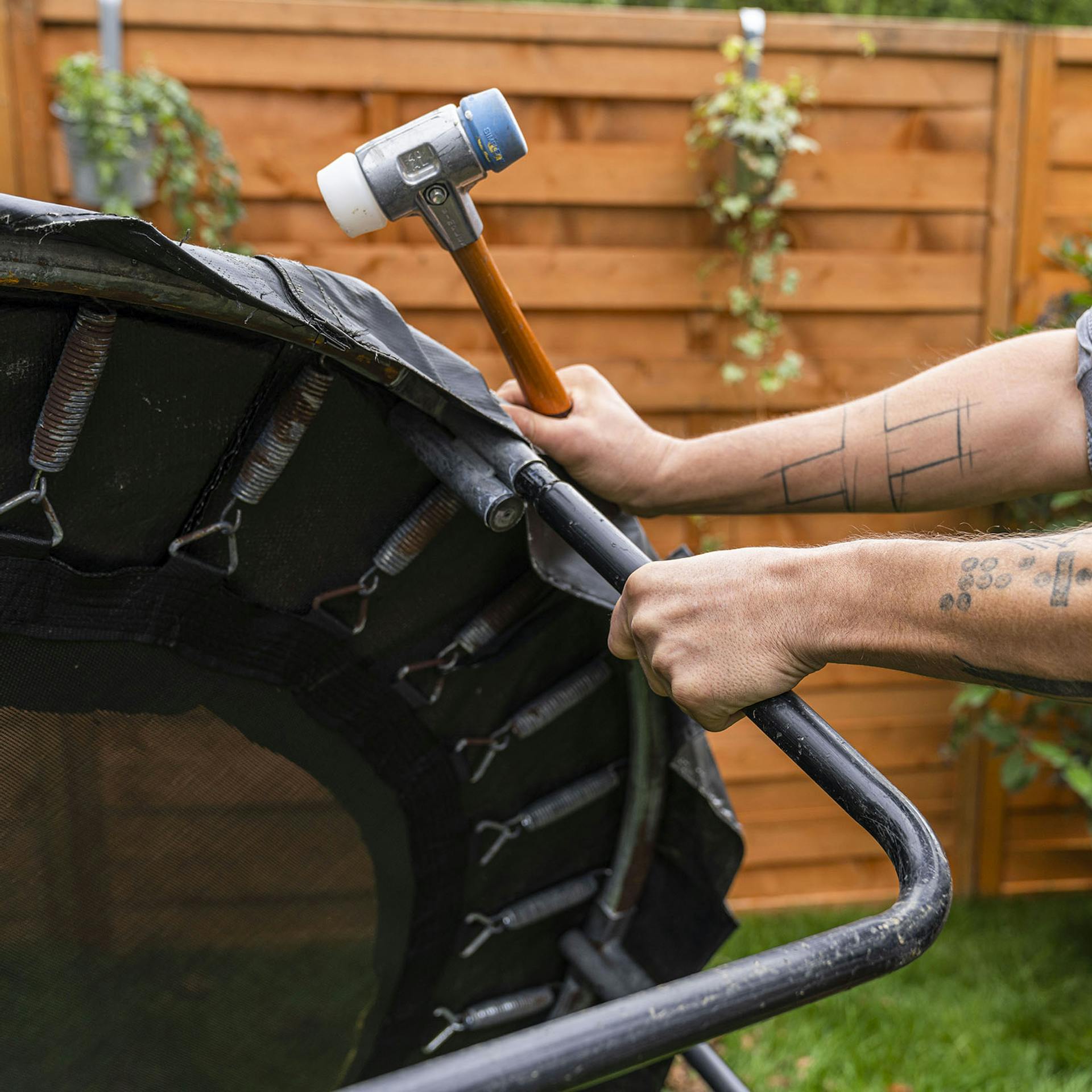Handwerker zieht an den Trampolinbeinen und hält einen Hammer in der Hand.