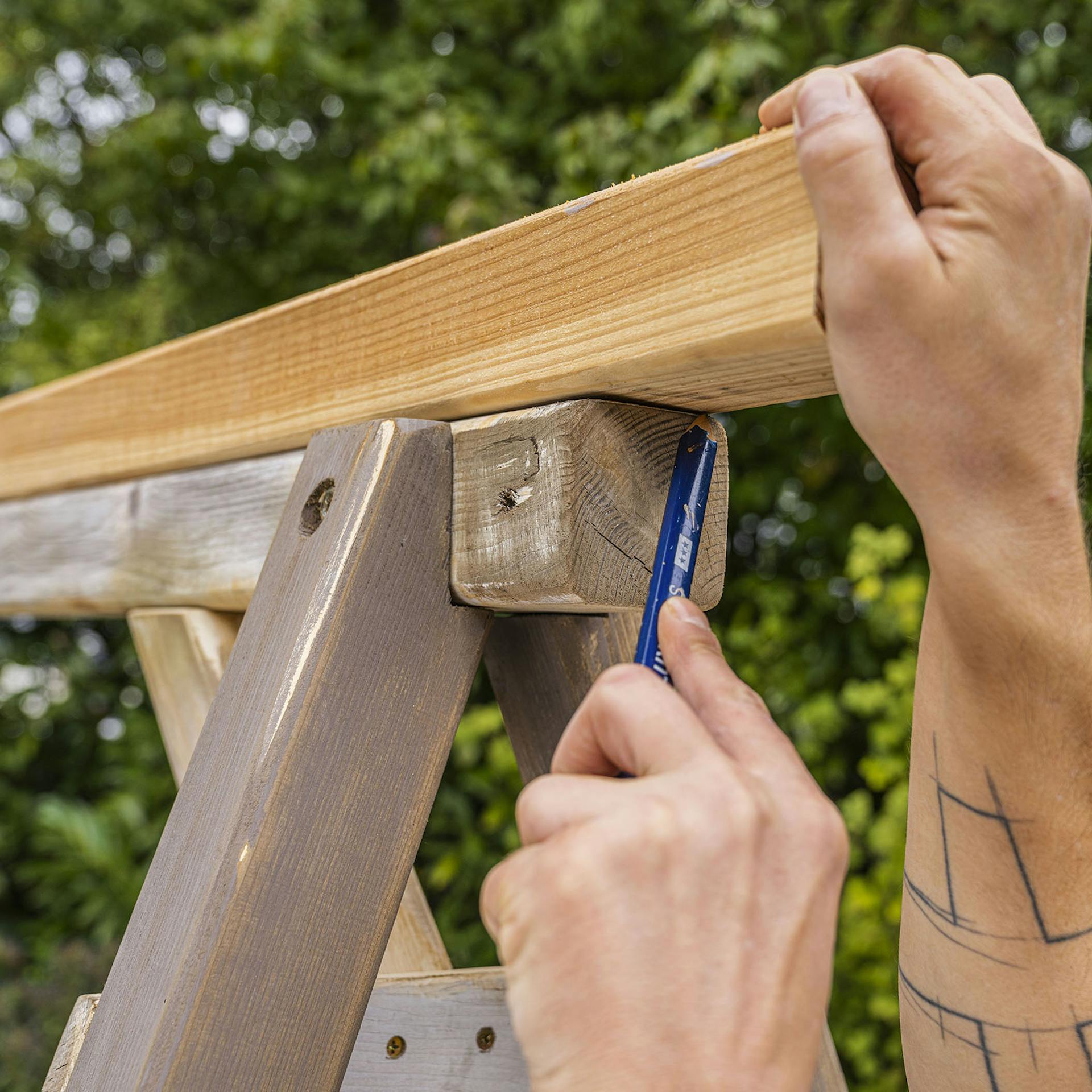 Handwerker zeichnet Maße auf einem Douglasienbalken an.