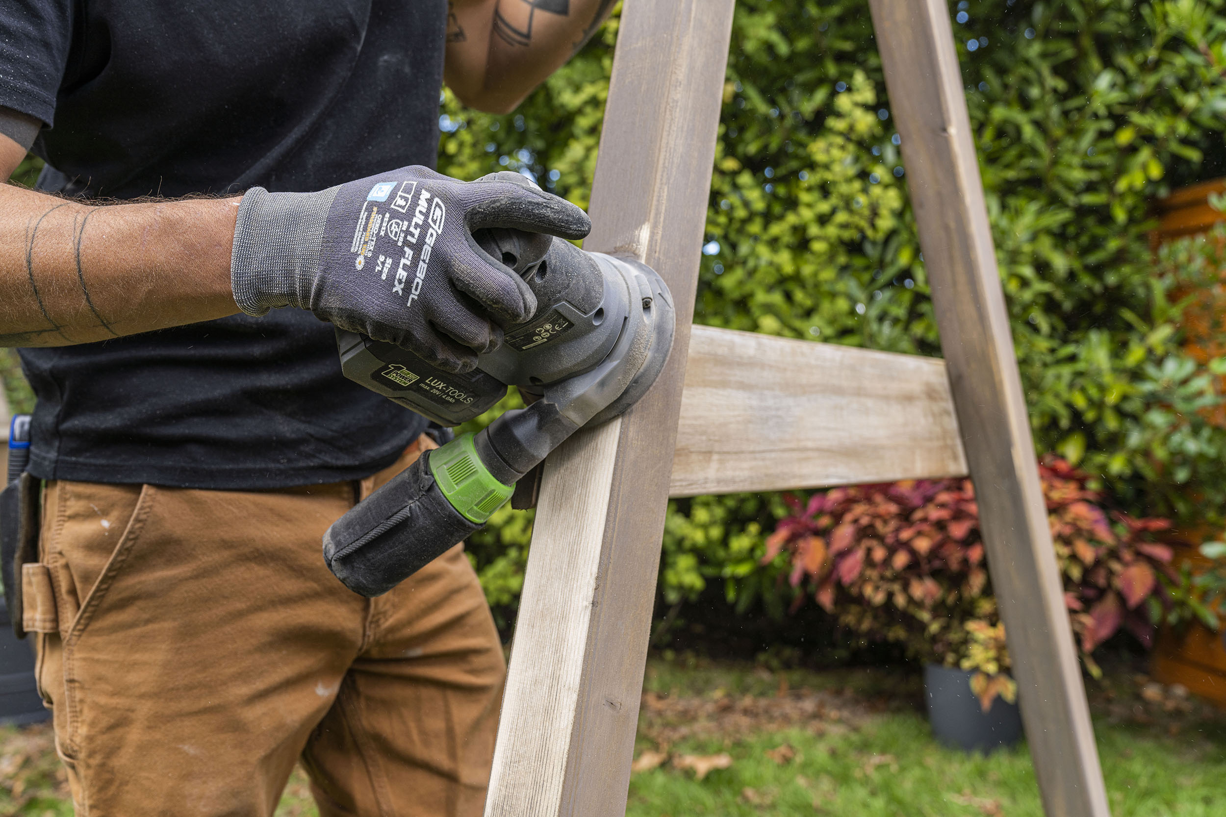 A mesterember akkumulátoros multicsiszolóval csiszolja a hintakeretet.