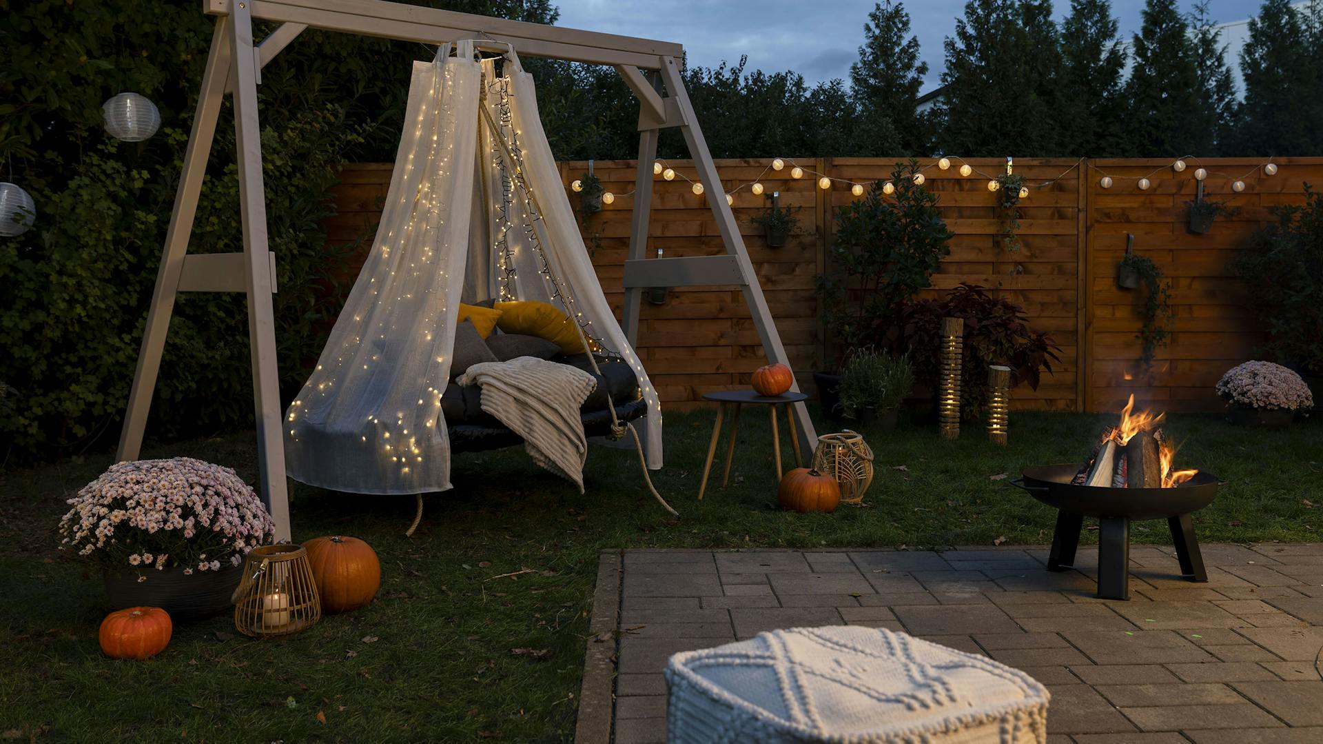 Trampolin-Hängebett steht bei Dämmerung im Garten und ist mit einer Lichterkette beschmückt.