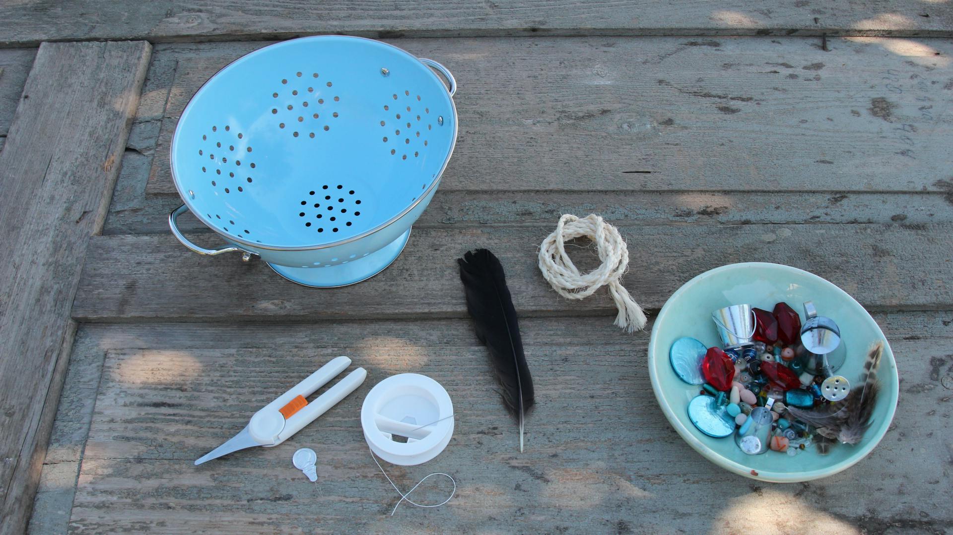 Blaues Metallsieb, Schnur, Schere, Feder und Perlen liegen auf einem Tisch.