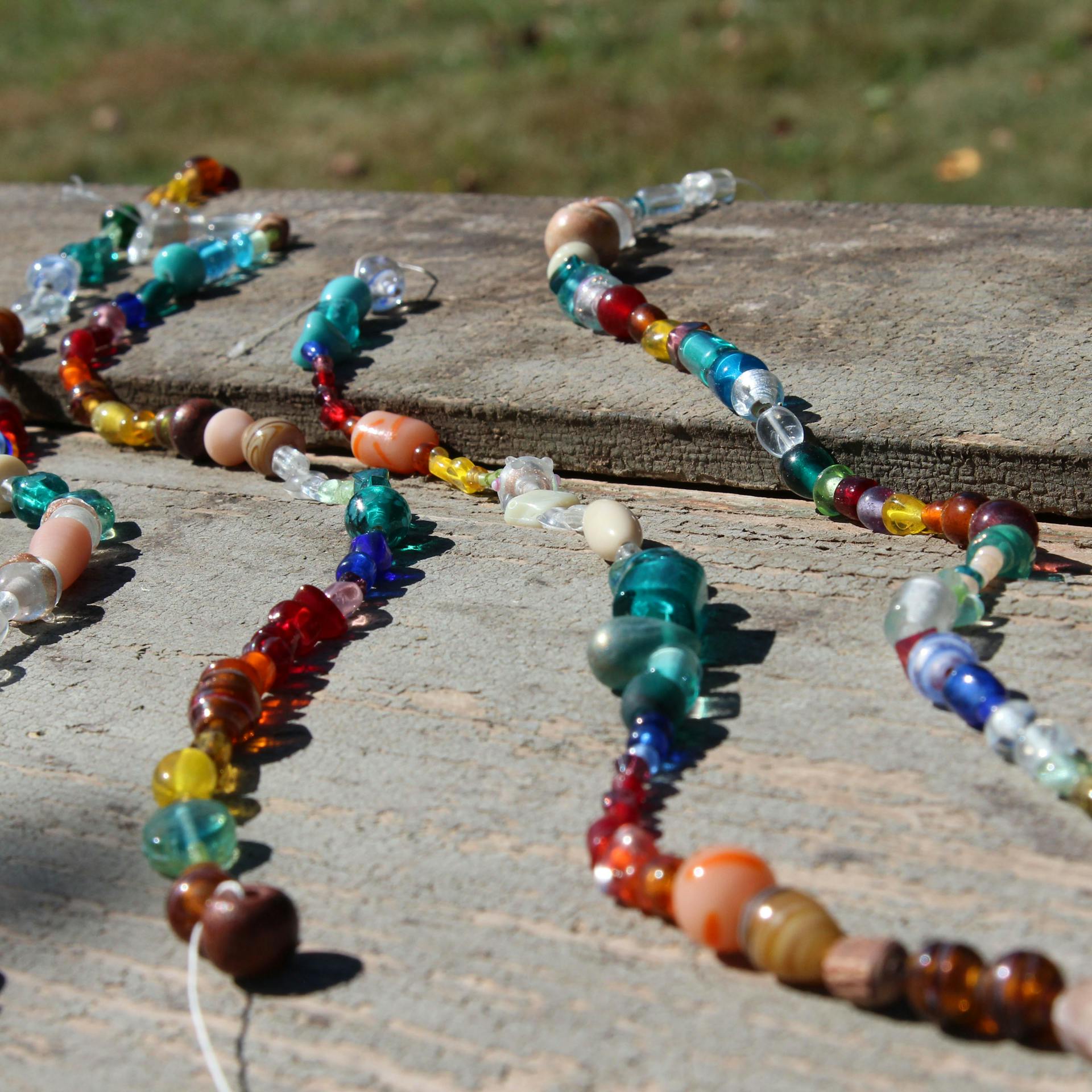 Perlenschnüre für Windspiel liegen ausgebreitet auf einem Holztisch im Garten.