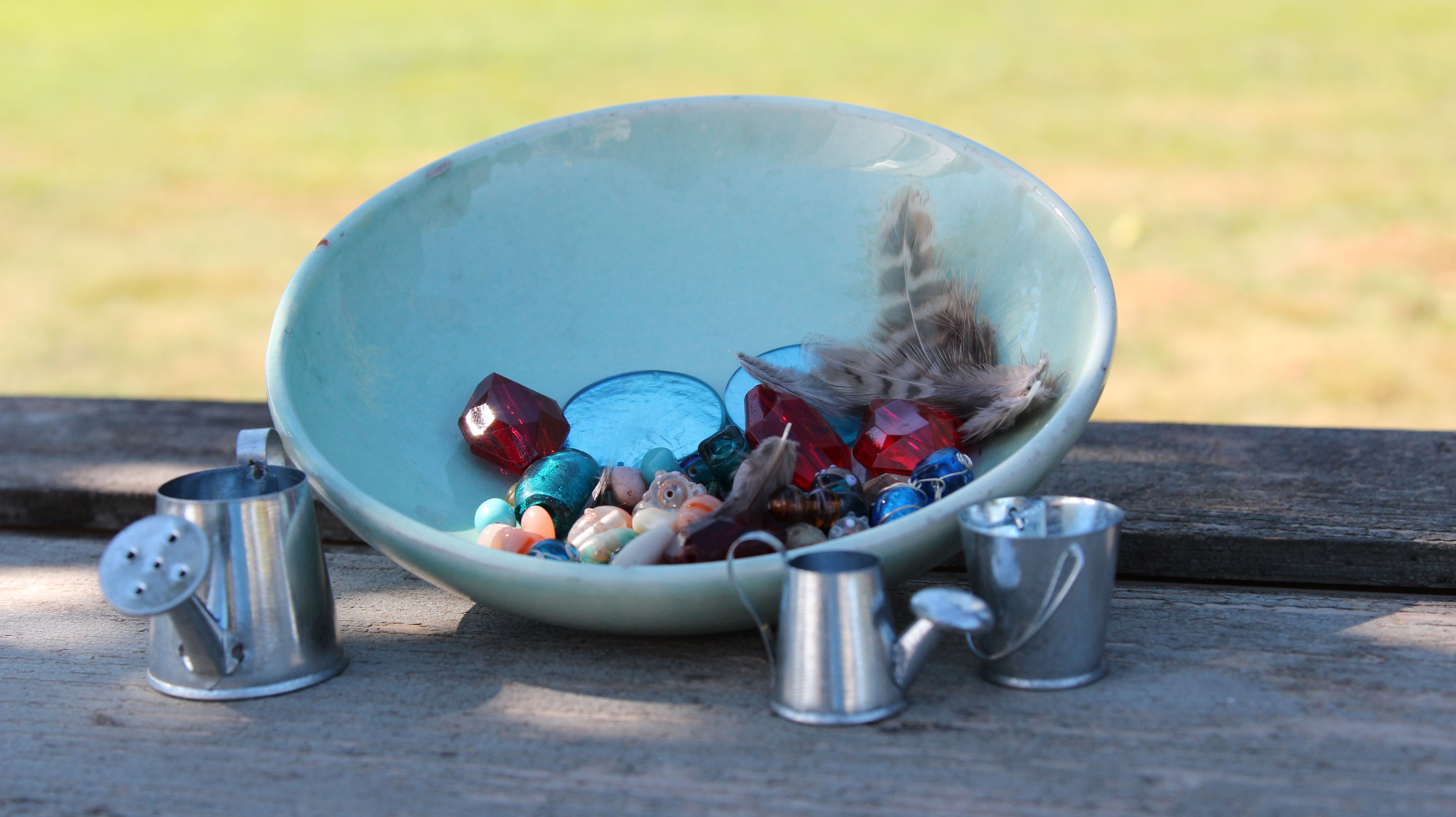 Ciotola con perle, oggetti decorativi e piume su un tavolo di legno.