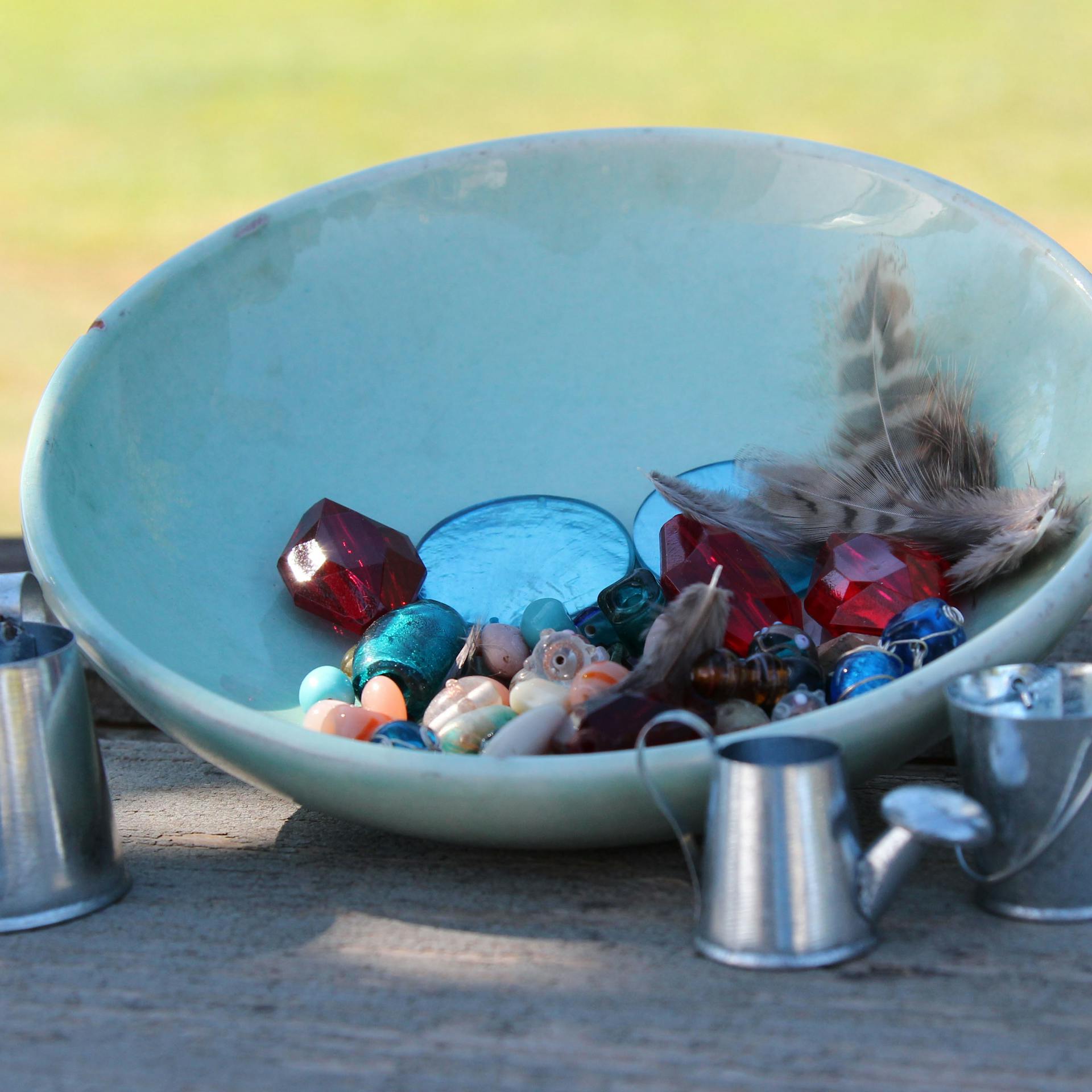 Schale mit Perlen, Dekoartikeln und Federn liegt auf Holztisch.