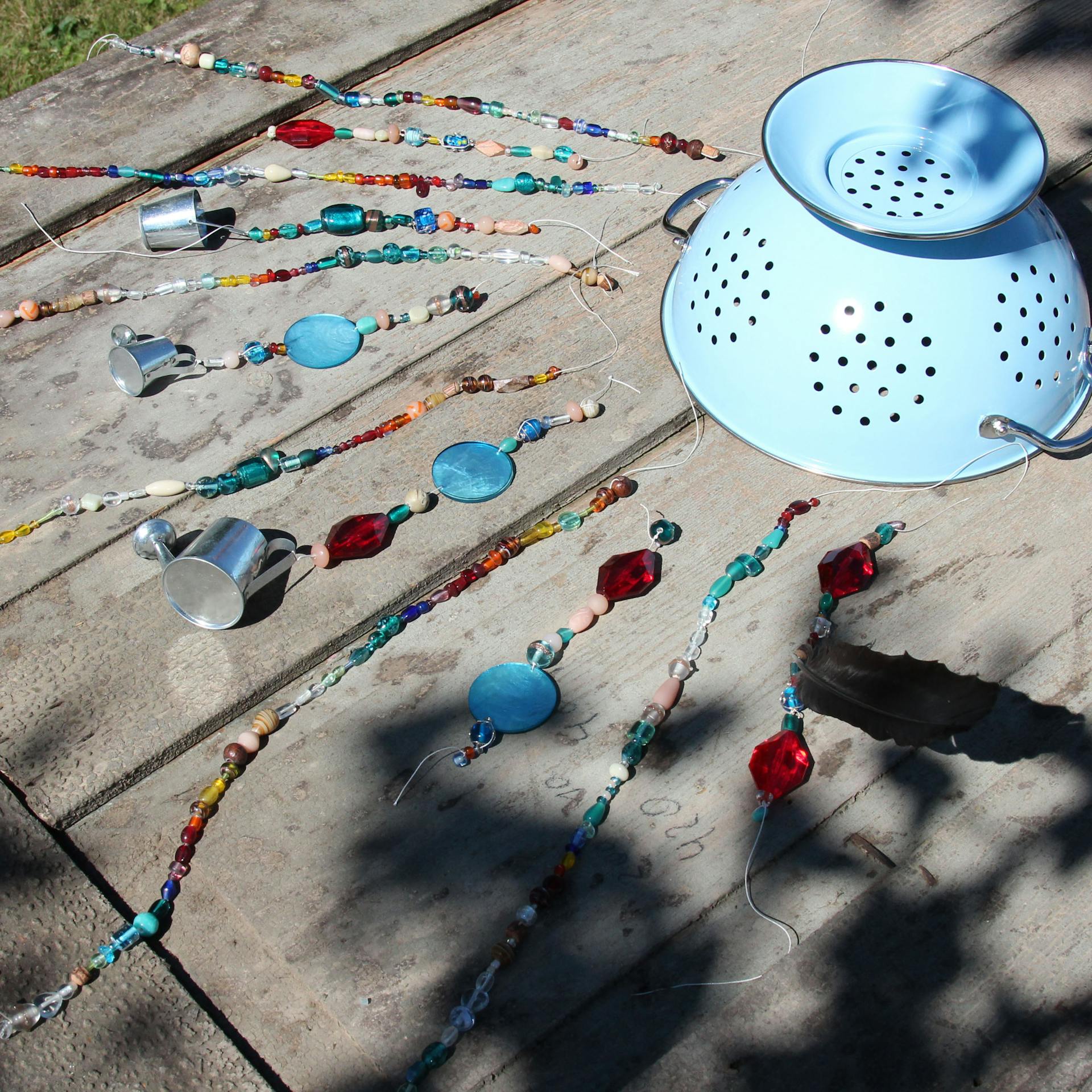 Dekorierte Ketten und Troddeln liegen nebeneinander aufgereiht neben Nudelsieb auf Holztisch.