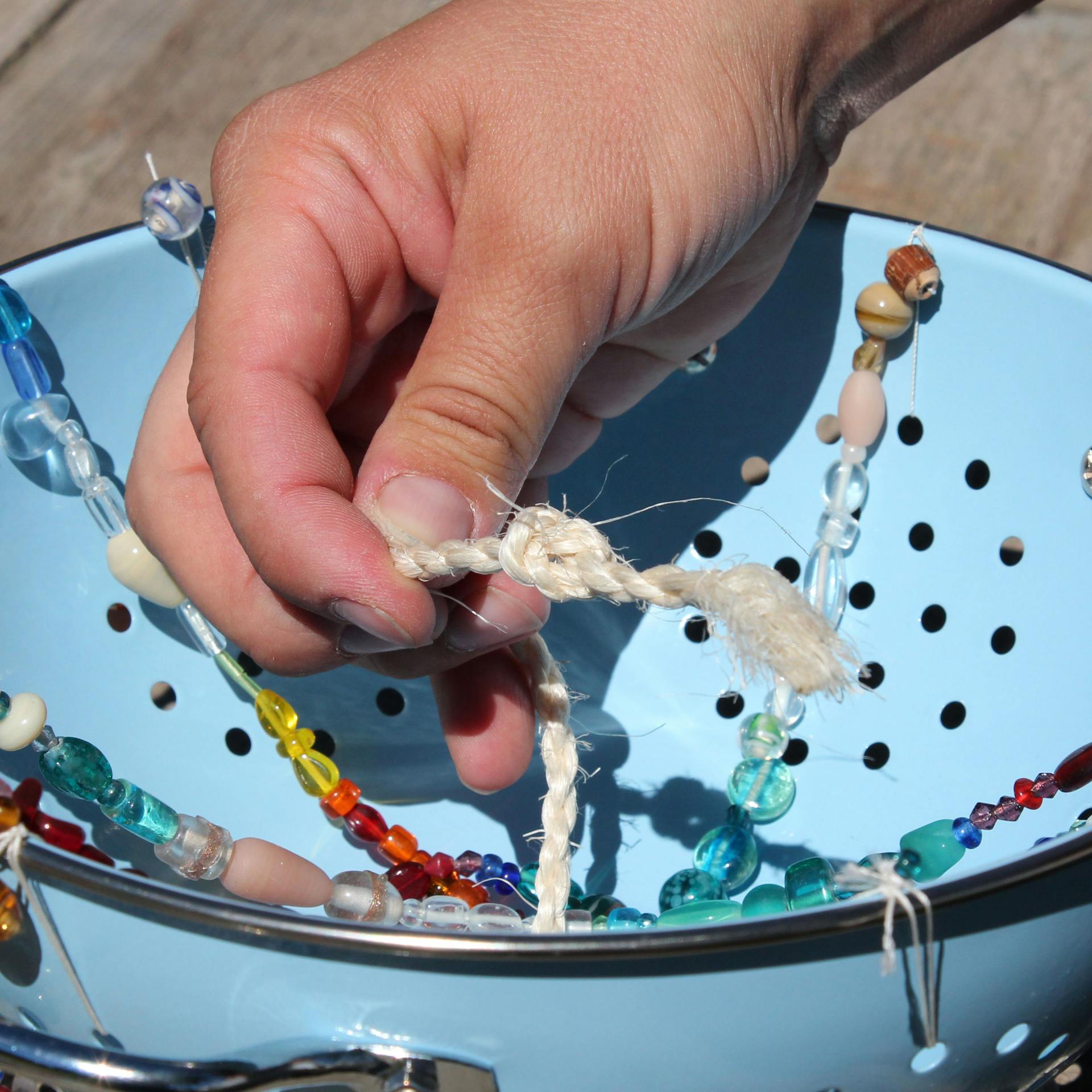 Heimwerker verknotet Sisal-Seil an Nudelsieb, das zum Windspiel dekoriert wurde.