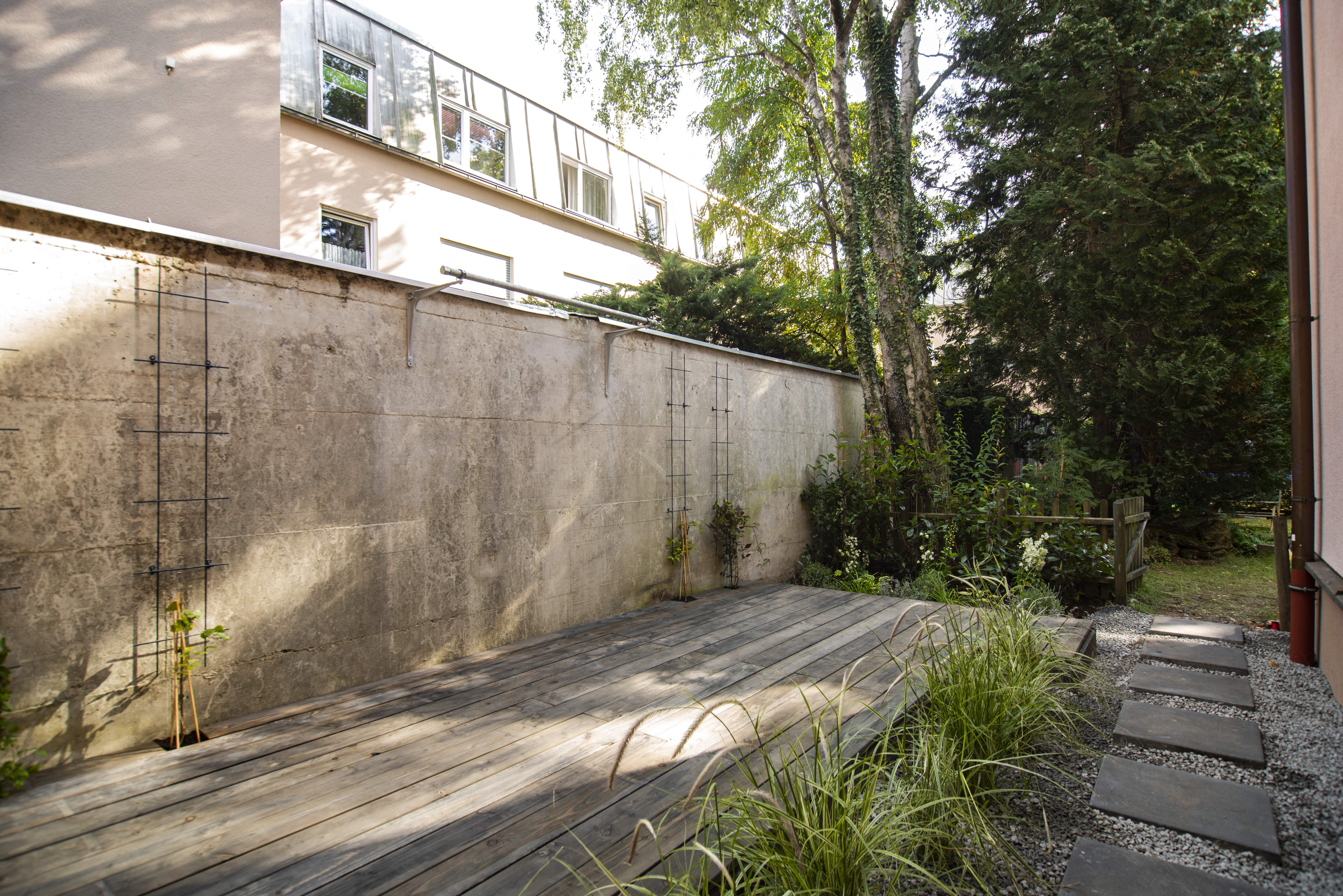 Holzterrasse neben Mauer und Gartenweg