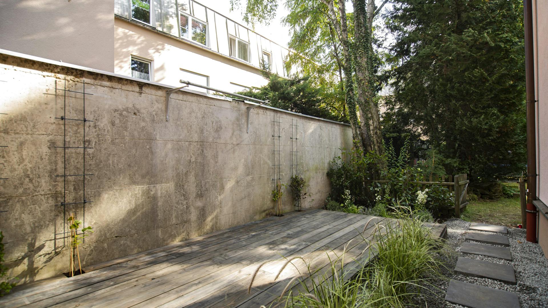 Holzterrasse neben Mauer und Gartenweg