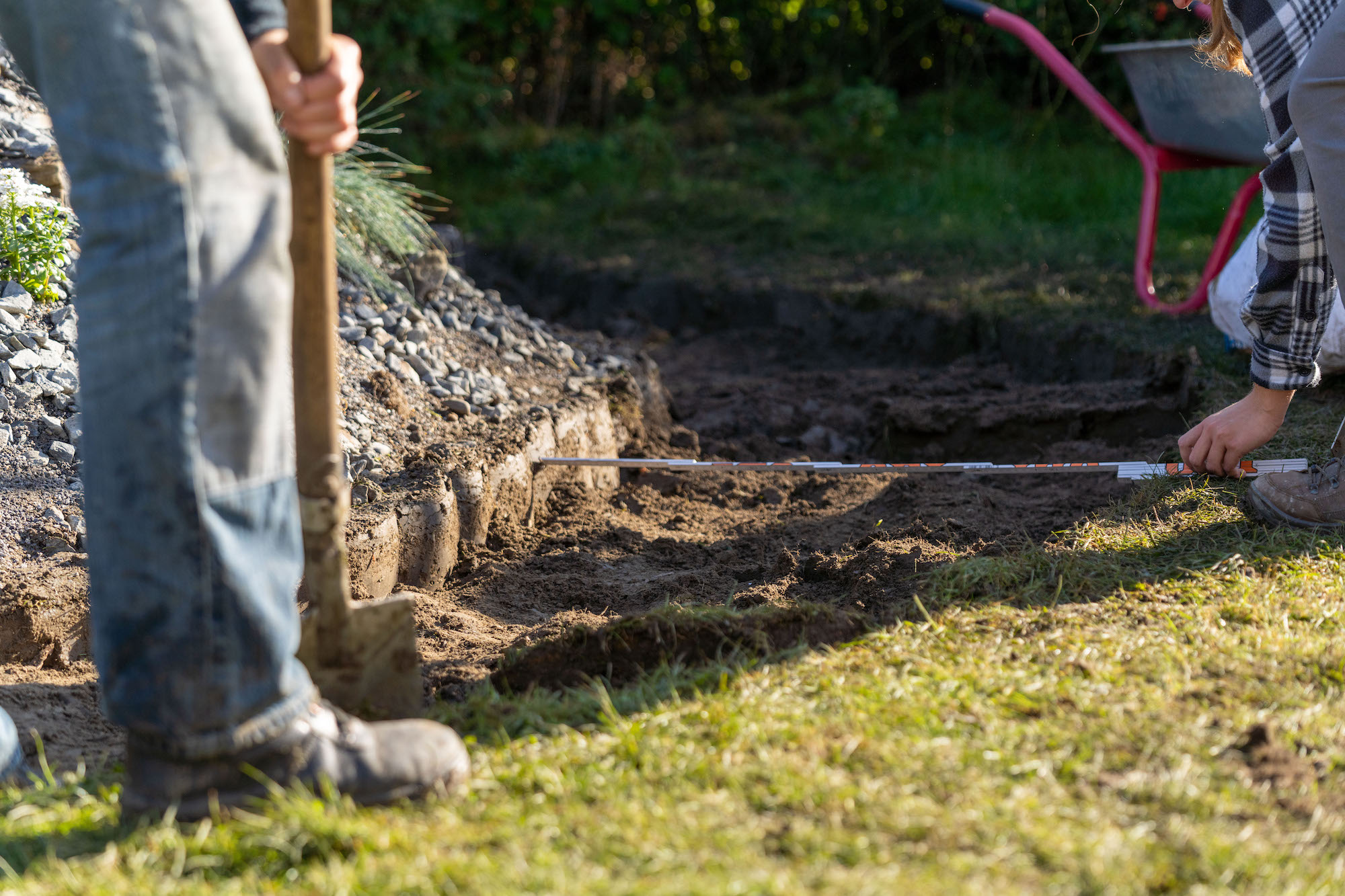 Person hält Zollstock über ausgehobenen Gartenweg