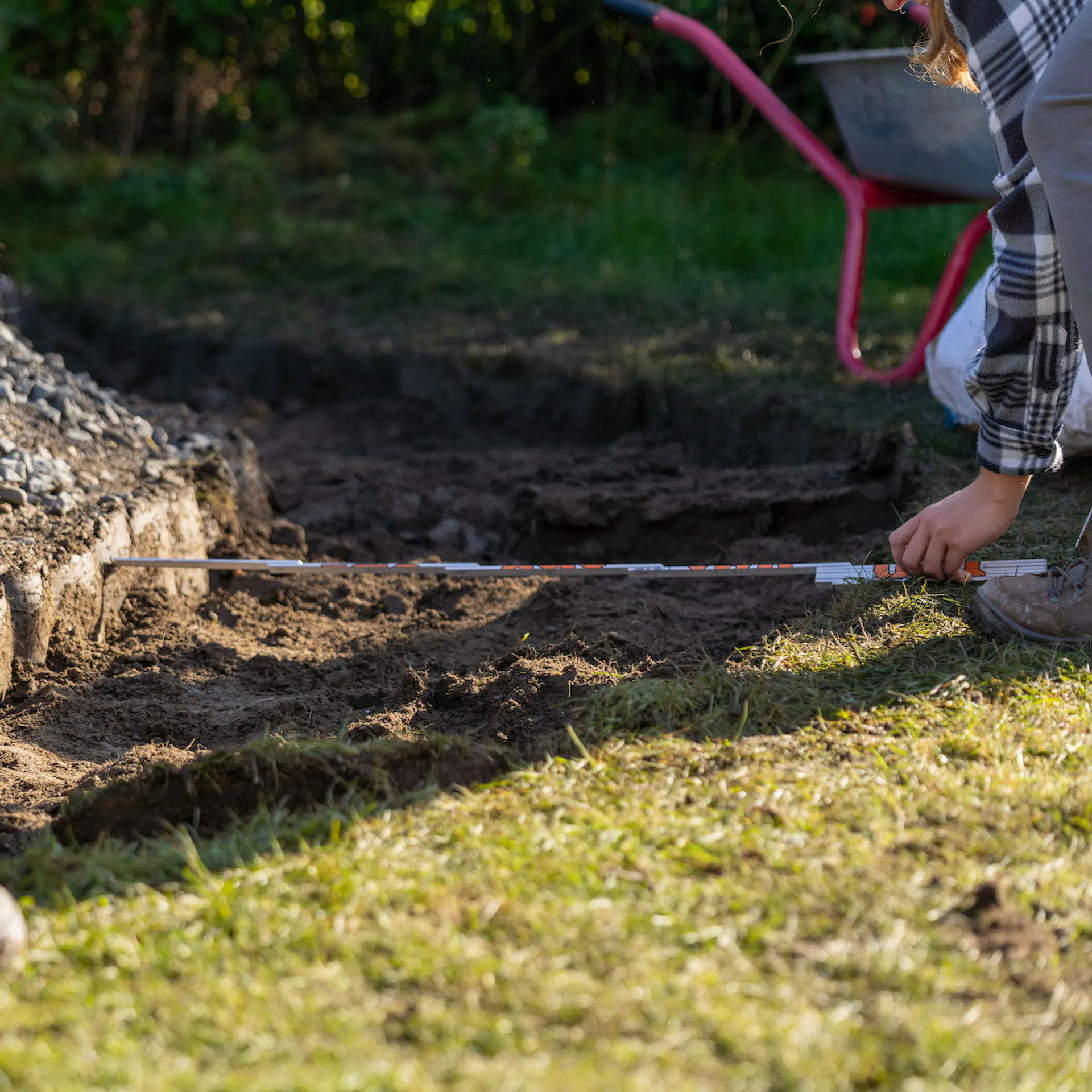 Person hält Zollstock über ausgehobenen Gartenweg
