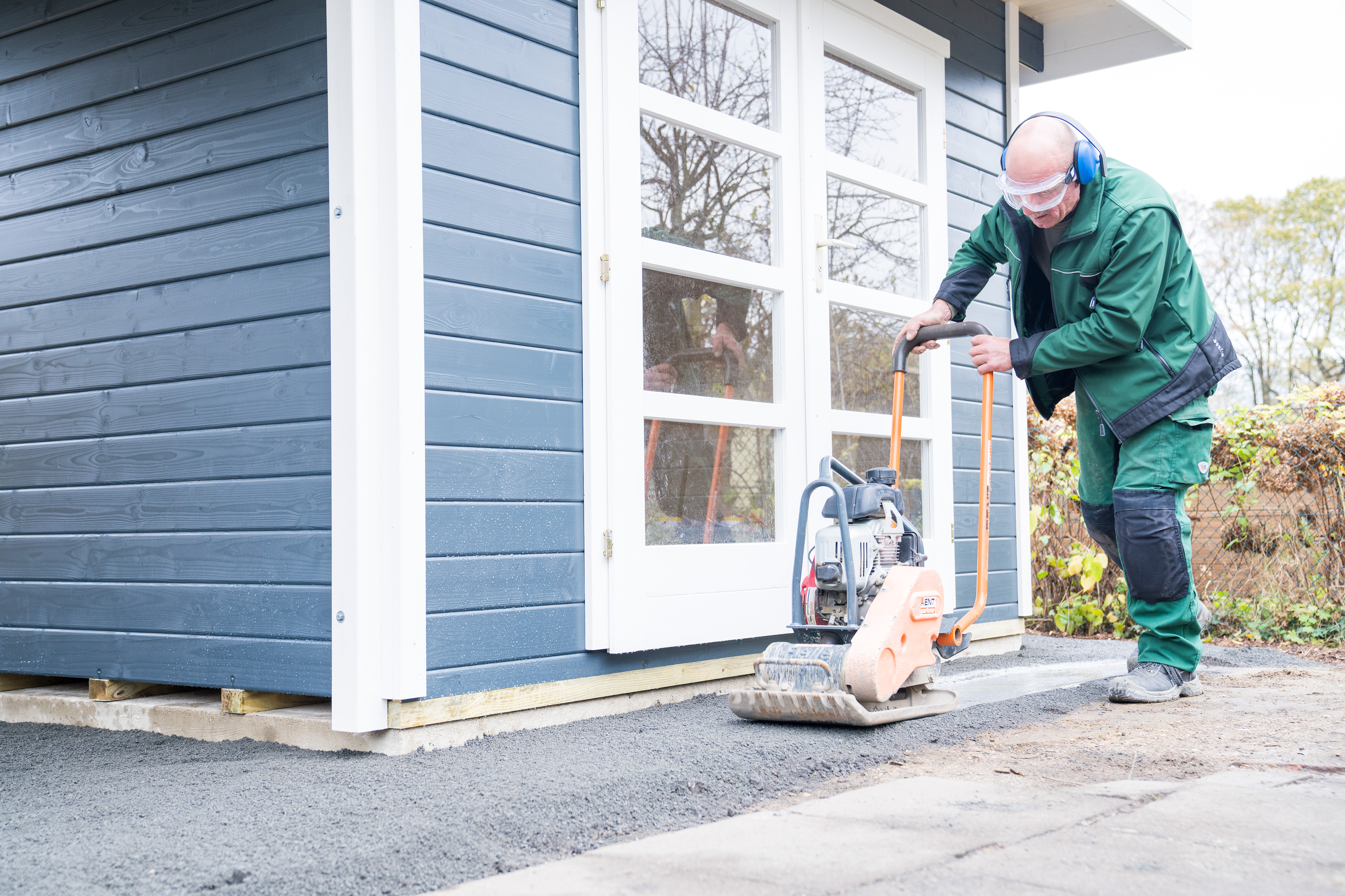 Egy ember egy döngölővel tömöríti a kerti ház körüli zúzalékot.