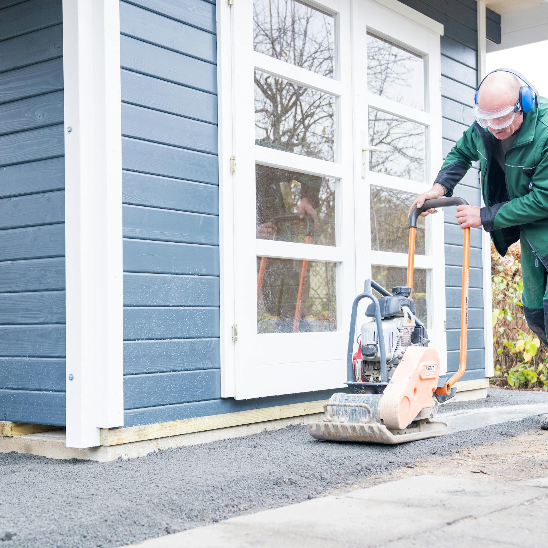 Egy ember egy döngölővel tömöríti a kerti ház körüli zúzalékot.
