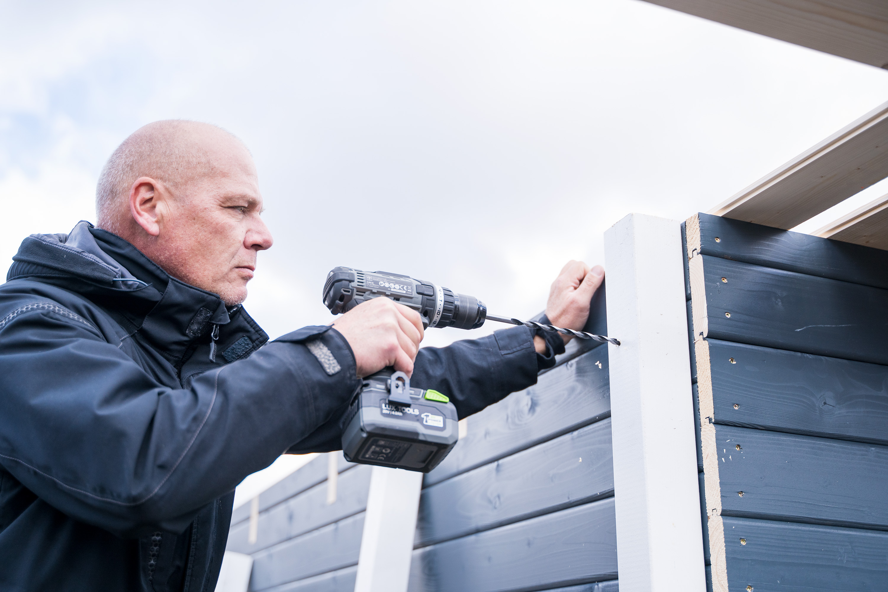 Egy ember előfuratokat készít az oldaltető sarokoszlopai számára.