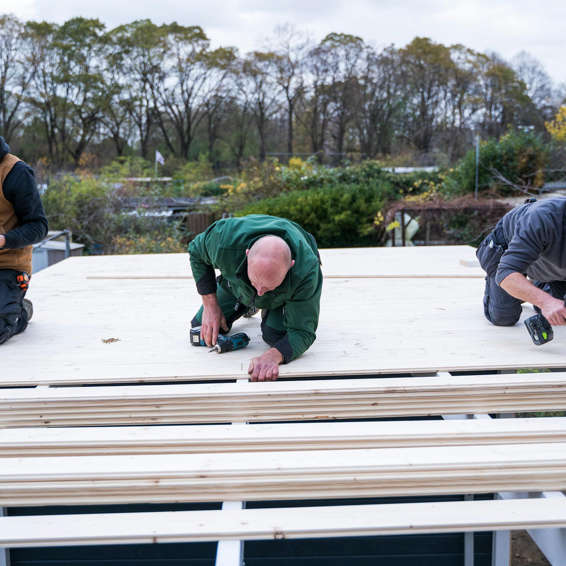 Három ember lefedi a kerti ház oldaltető szerkezetét.