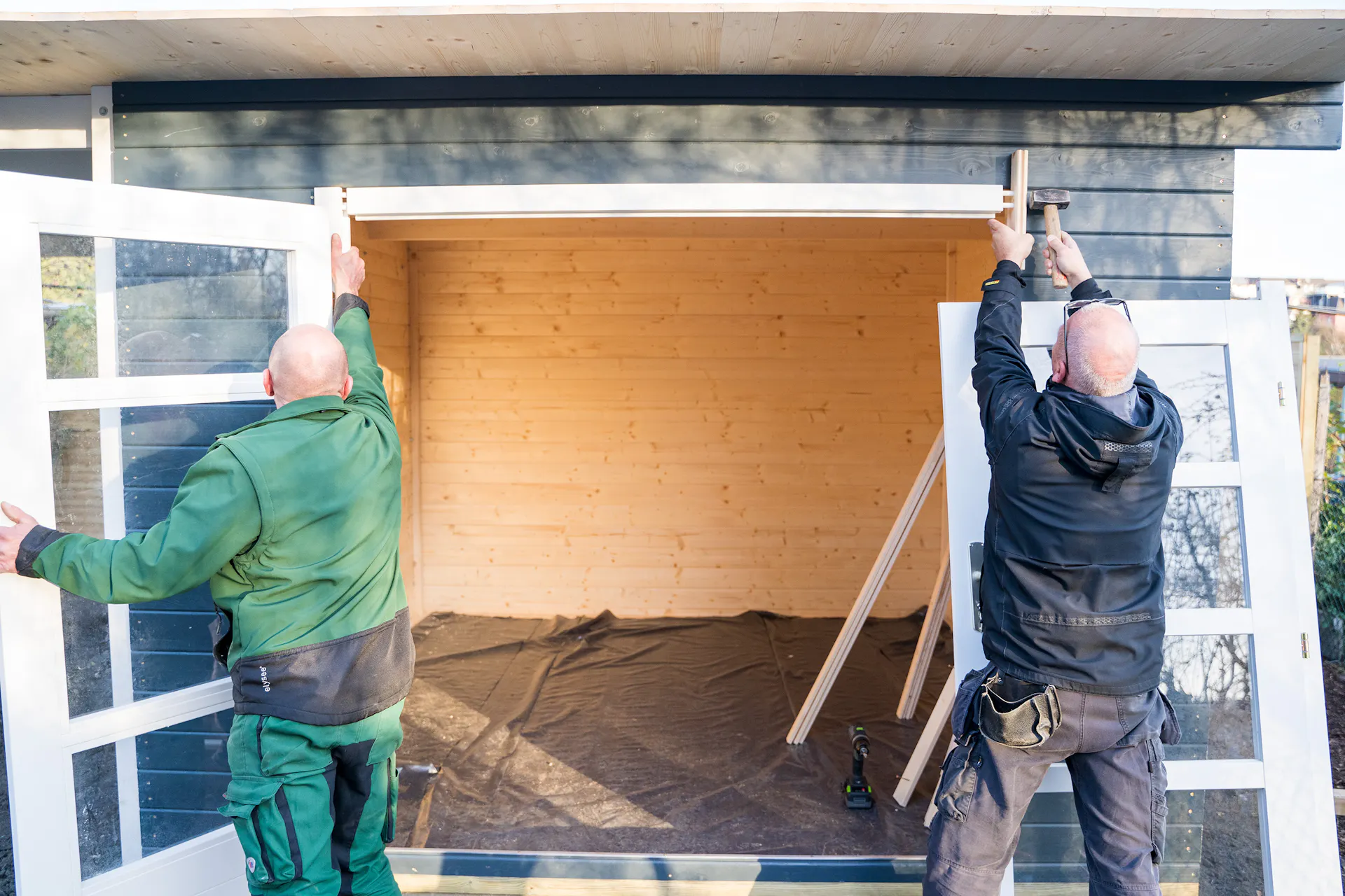 Due persone fissano il battente superiore della porta con un pezzo di legno.