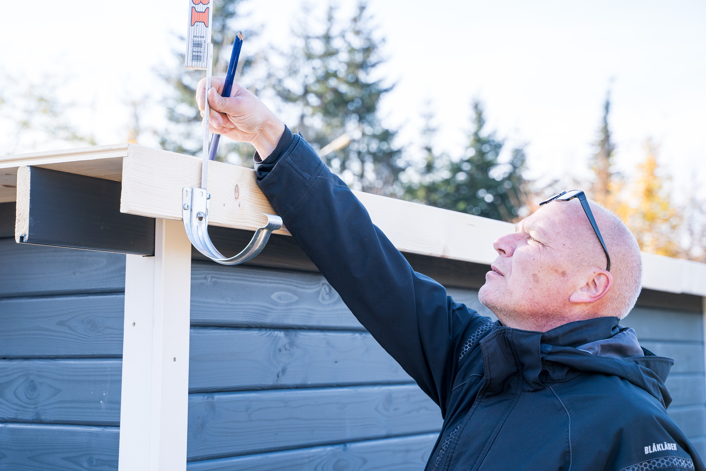 Egy ember méretet vesz az ereszcsatorna tartójánál a megfelelő lejtés beállításához.
