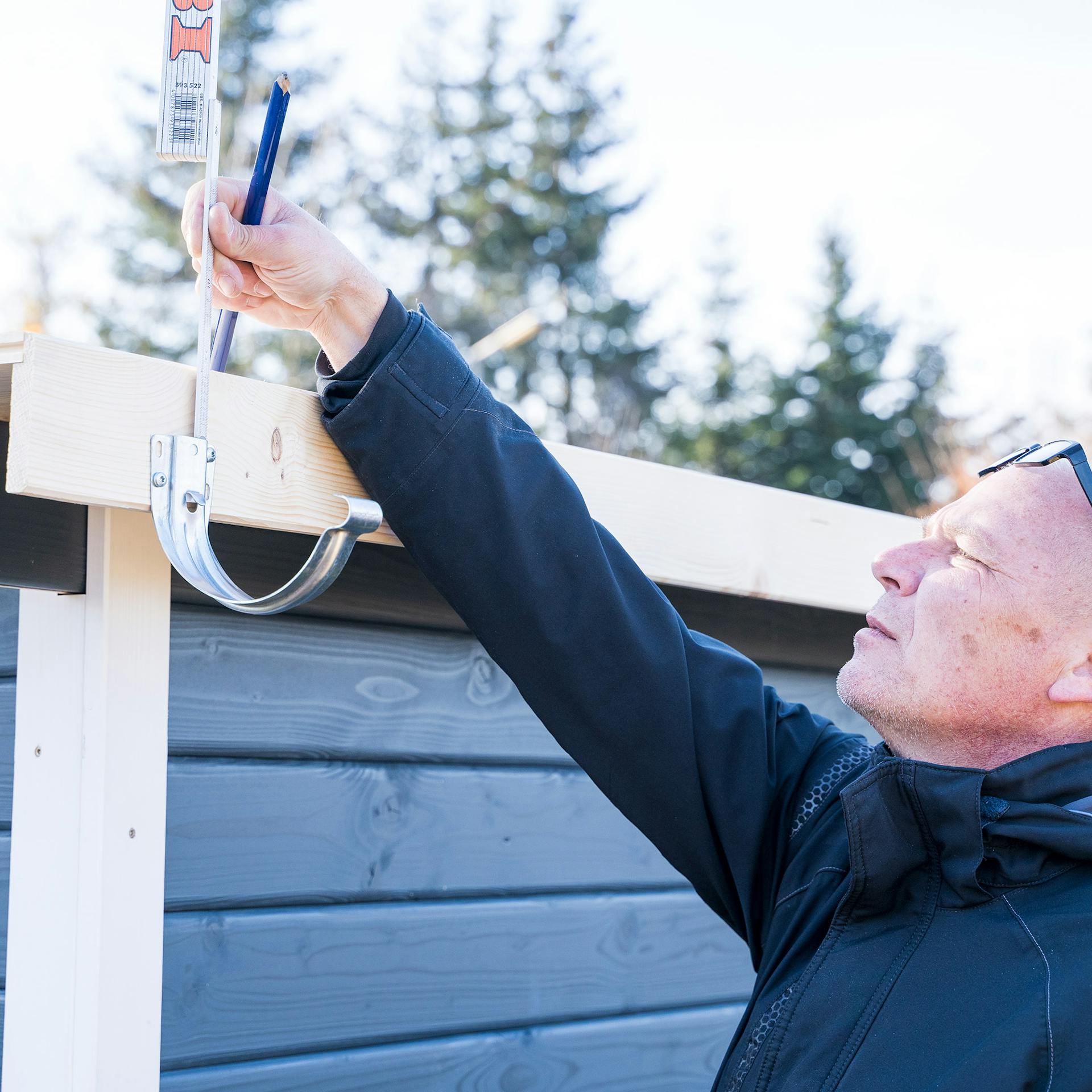 Egy ember méretet vesz az ereszcsatorna tartójánál a megfelelő lejtés beállításához.