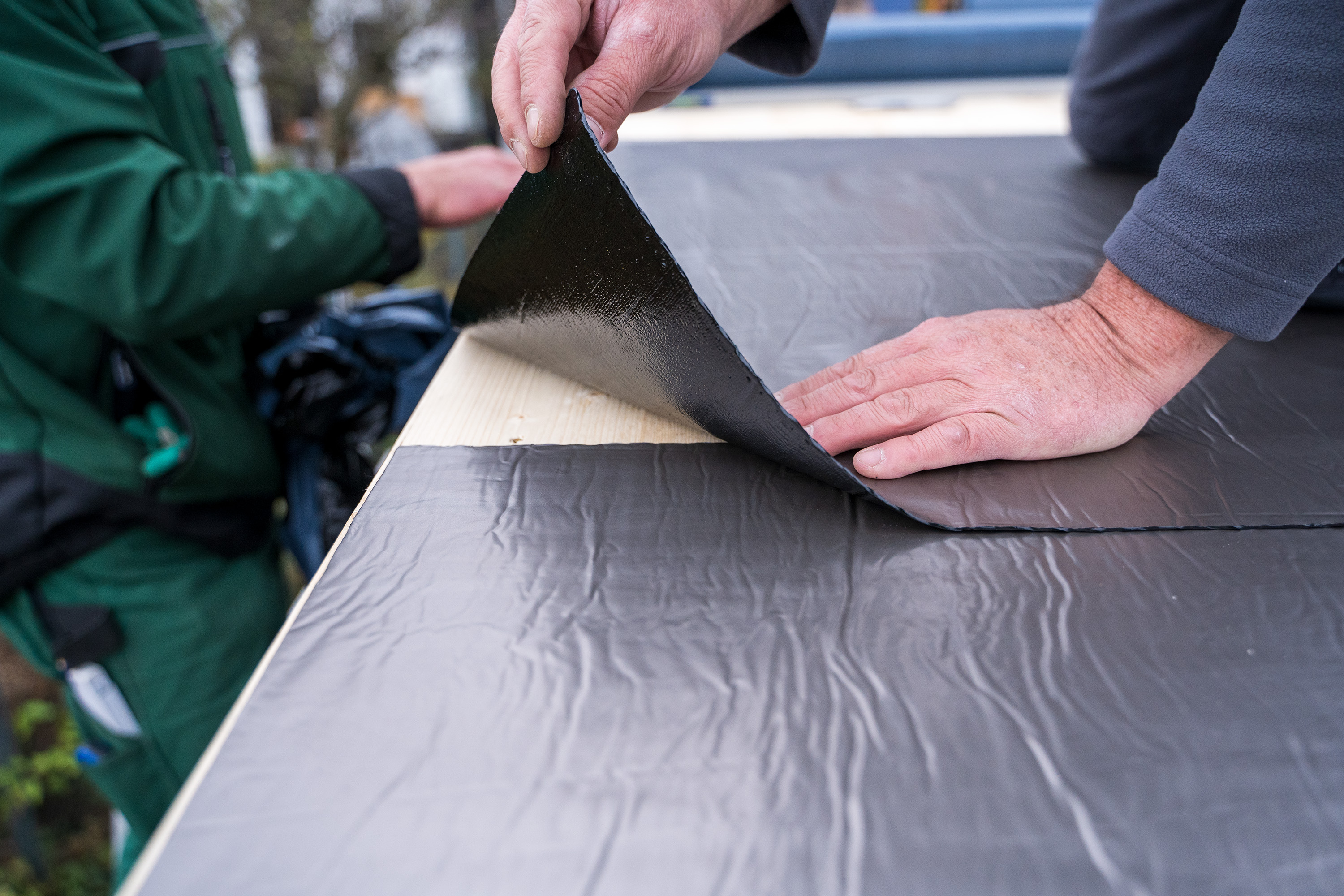 Egy ember bitumenes lemezeket fektet egymással átfedésben.