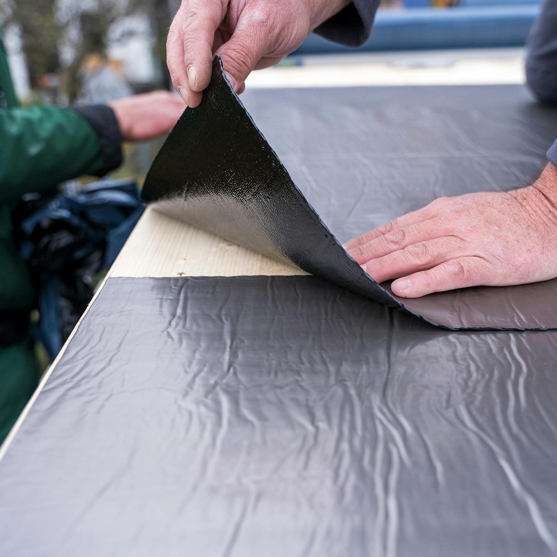 Egy ember bitumenes lemezeket fektet egymással átfedésben.