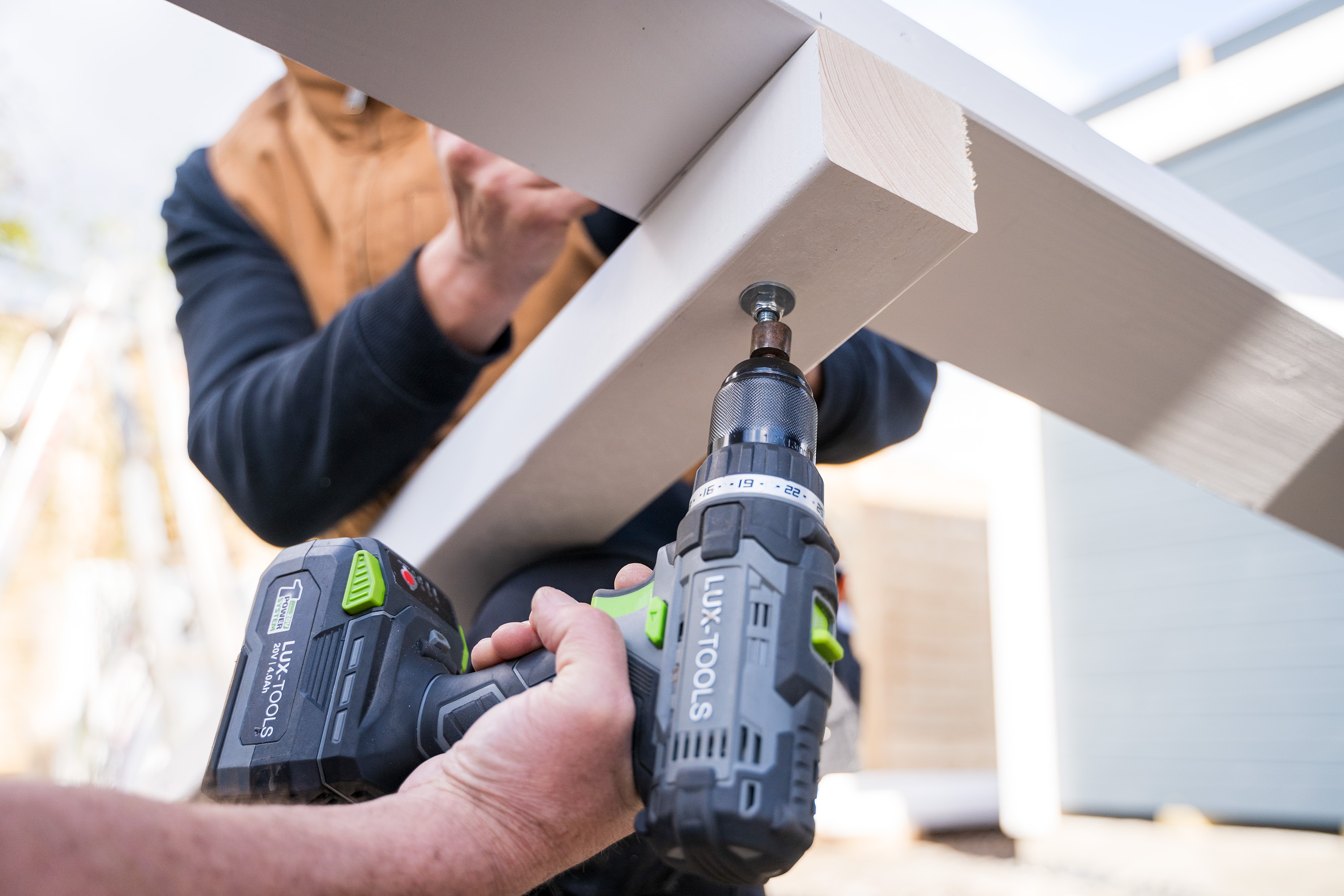 Egy ember keresztmerevítőket rögzít kapupántcsavarokkal a kerti ház sarokoszlopaihoz.