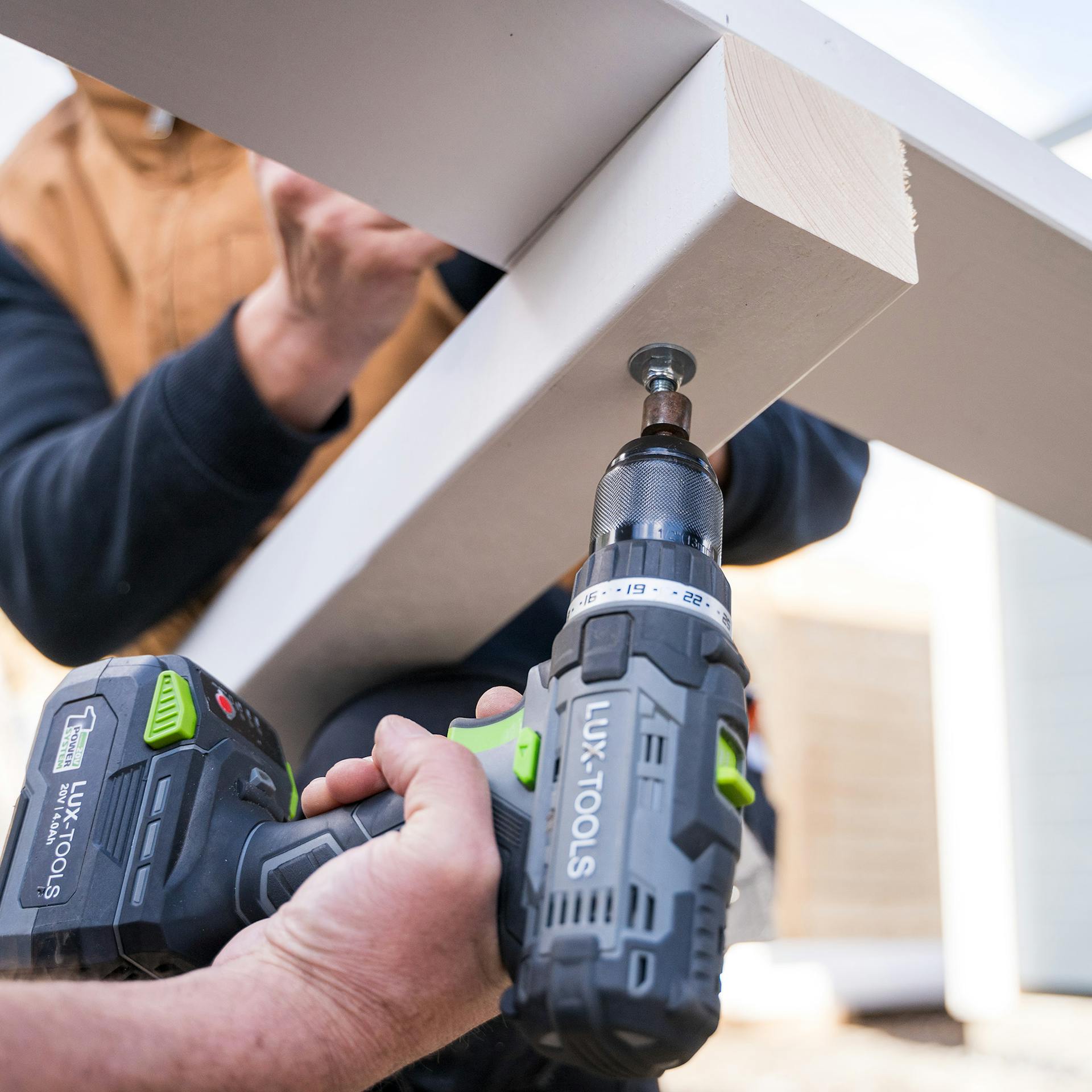 Egy ember keresztmerevítőket rögzít kapupántcsavarokkal a kerti ház sarokoszlopaihoz.