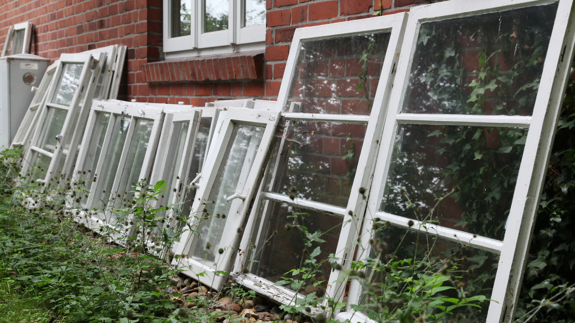 Alte Holzfenster lehnen an einer Hauswand.
