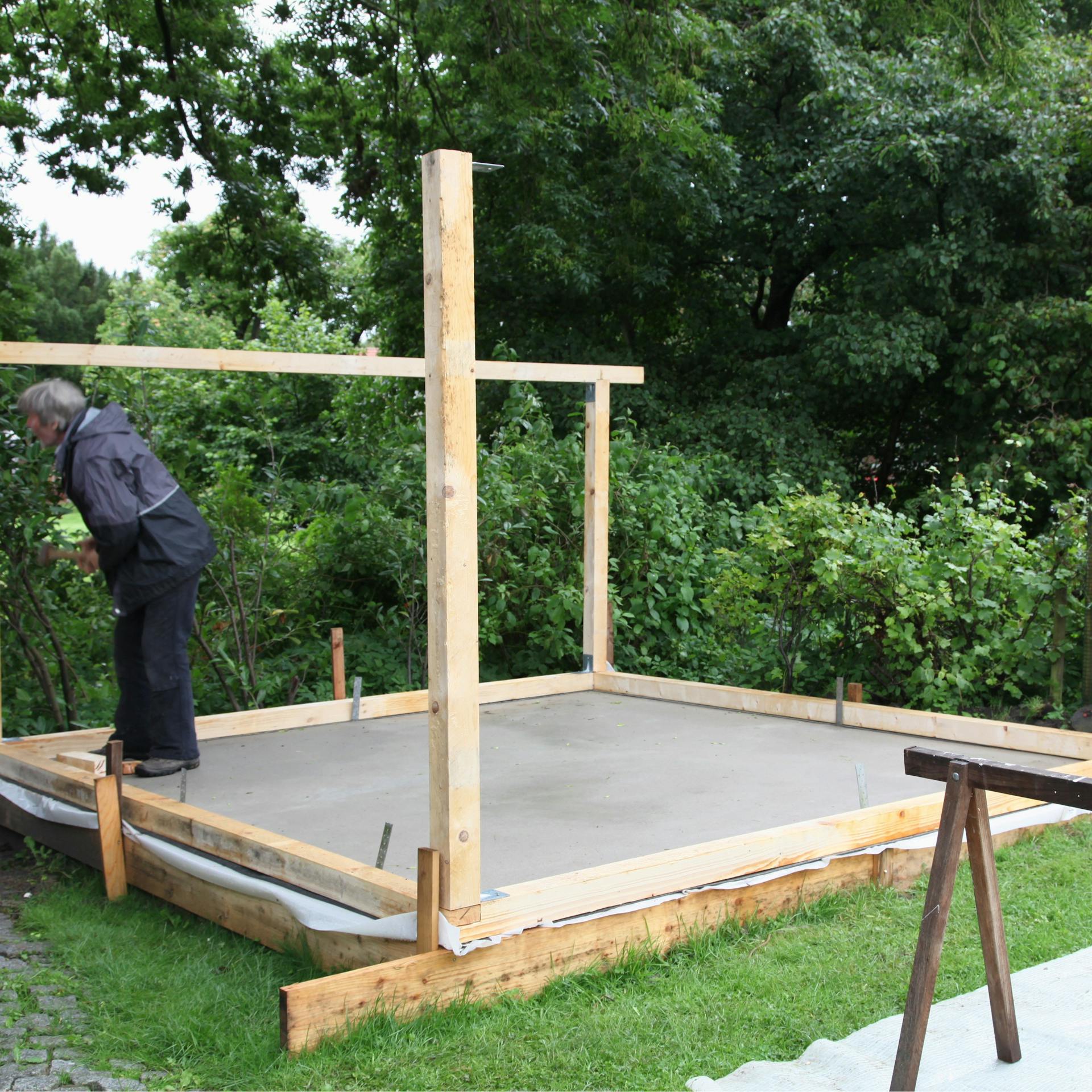 Egy férfi alapvázat szerel össze egy kerti ház alapozásán