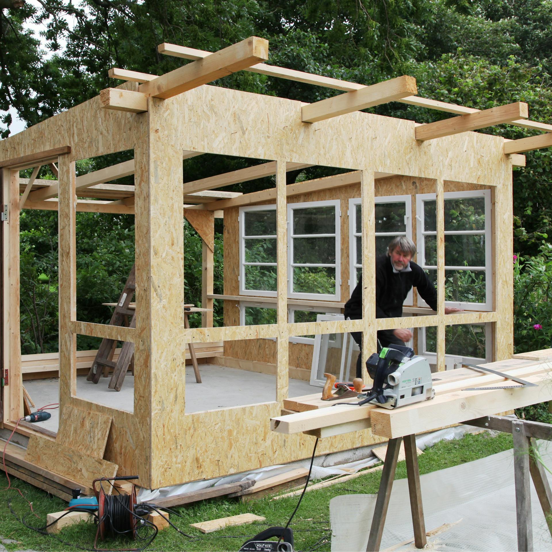 Egy férfi ablakokat épít be egy kerti házba.