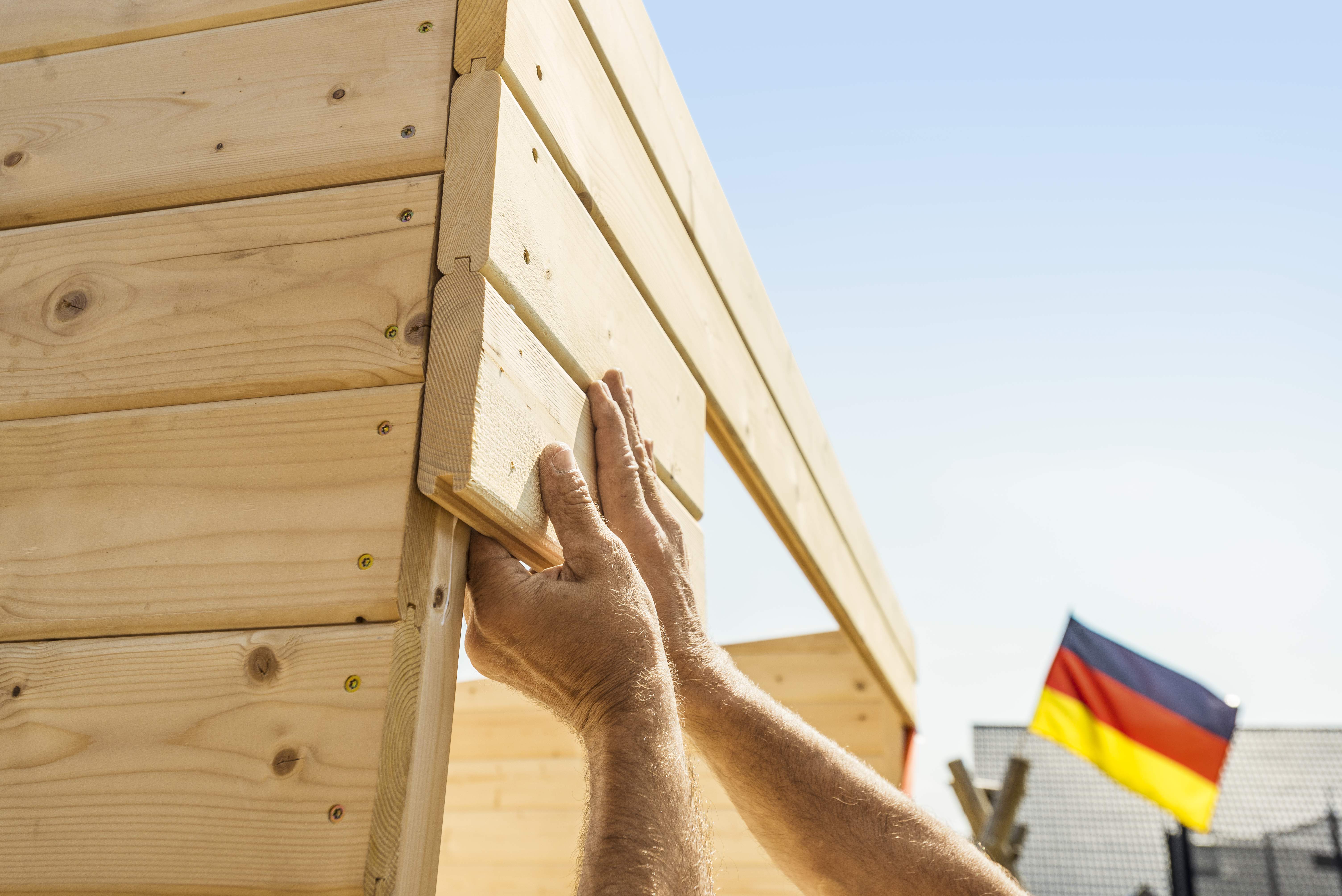 Eine Hand befestigt eine Latte an ein Gartenhaus.