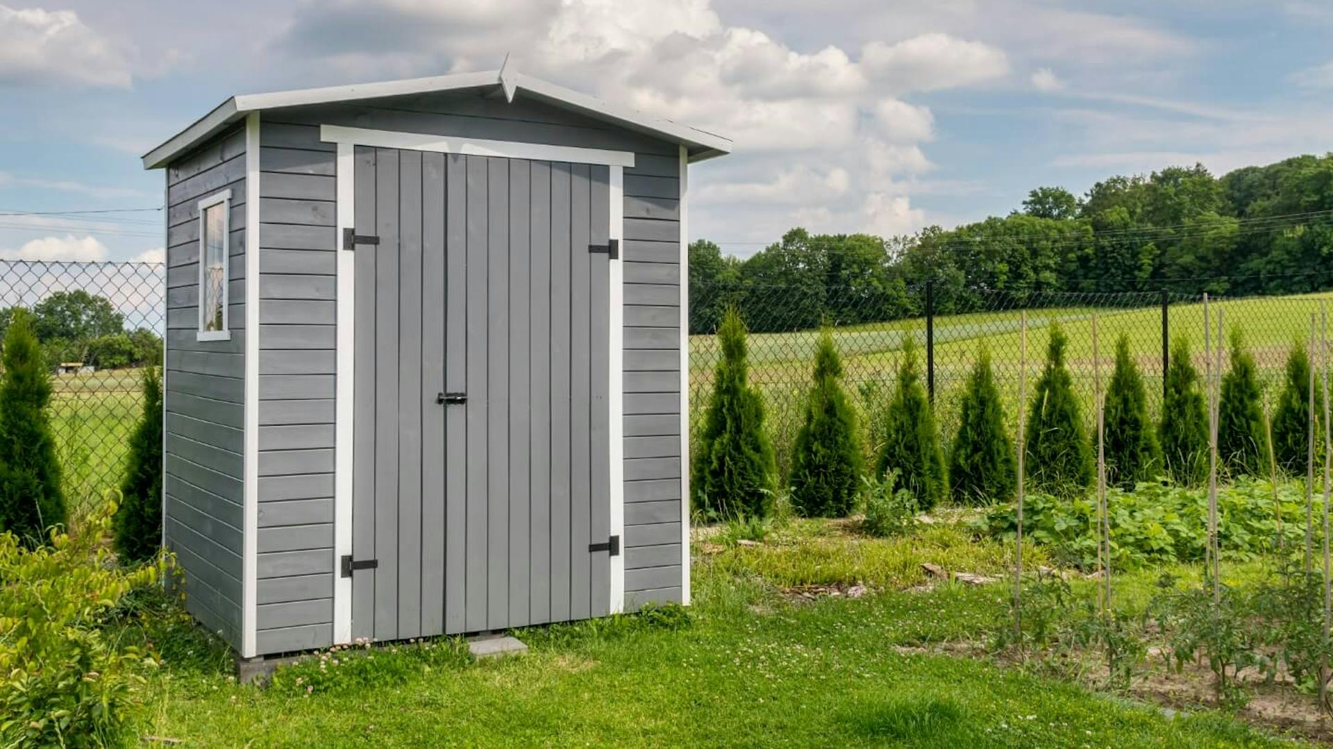 Grauer Geräteschuppen aus Holz im Garten neben Gartenzaun und Beeten